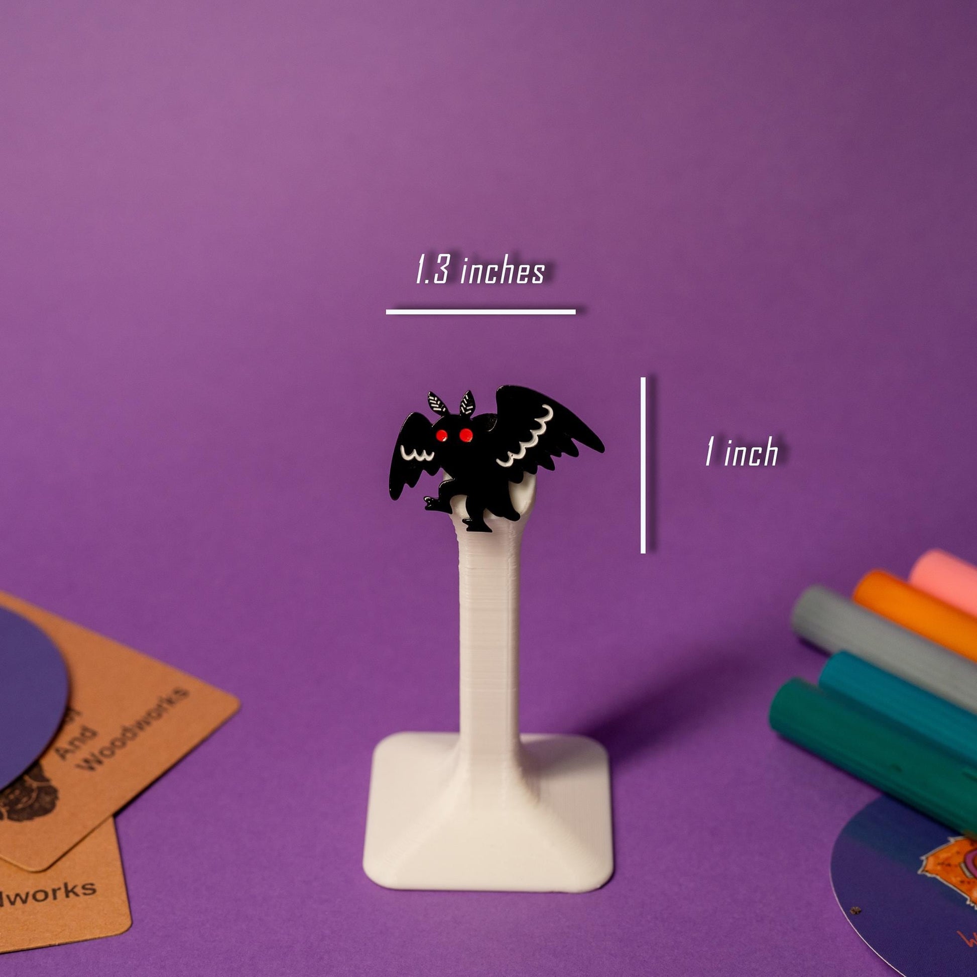 Mothman enamel pin displayed on a stand, highlighting the cryptid creature’s iconic silhouette.