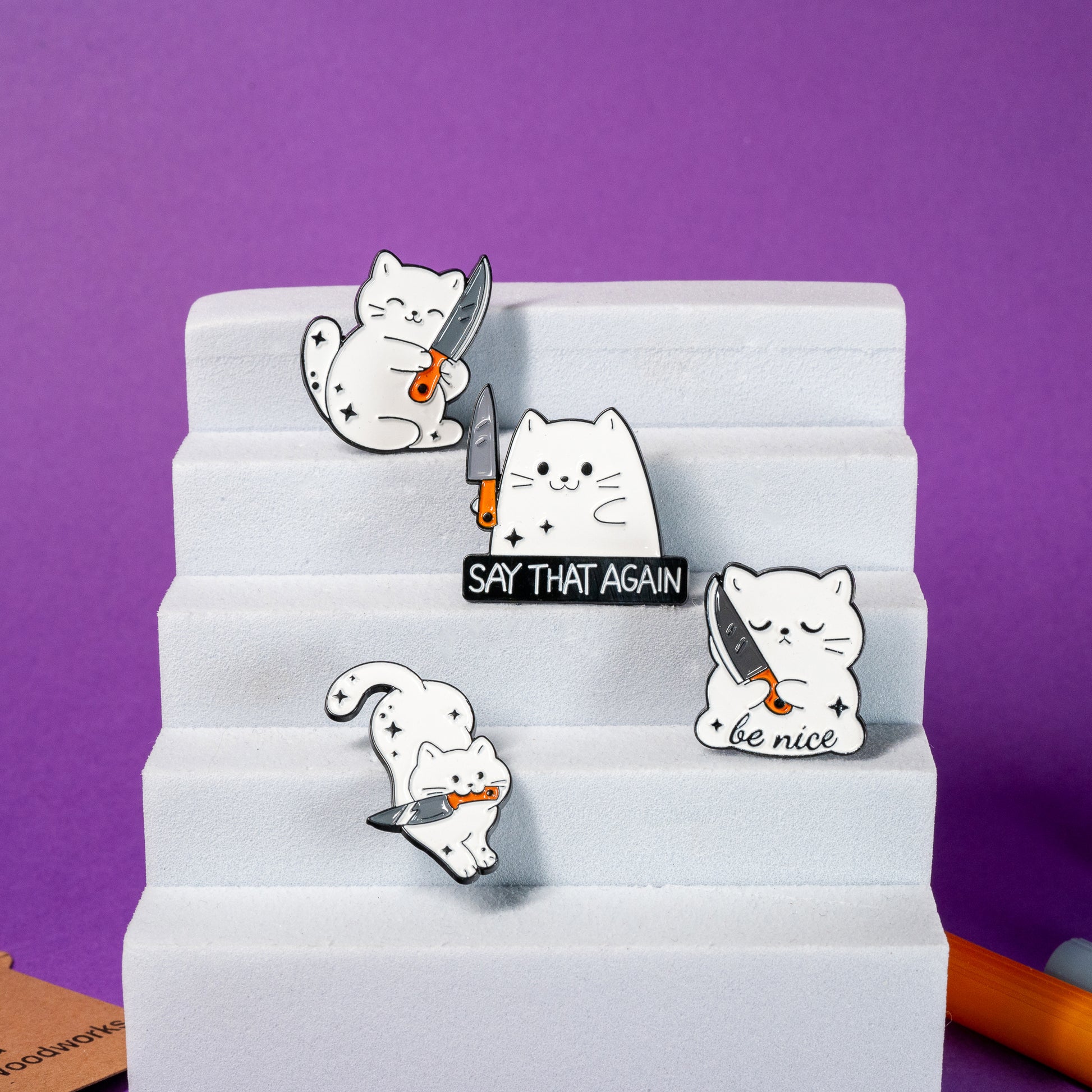 Complete collection of white cat enamel pins with humorous and quirky knife designs, perfect for cat lovers.