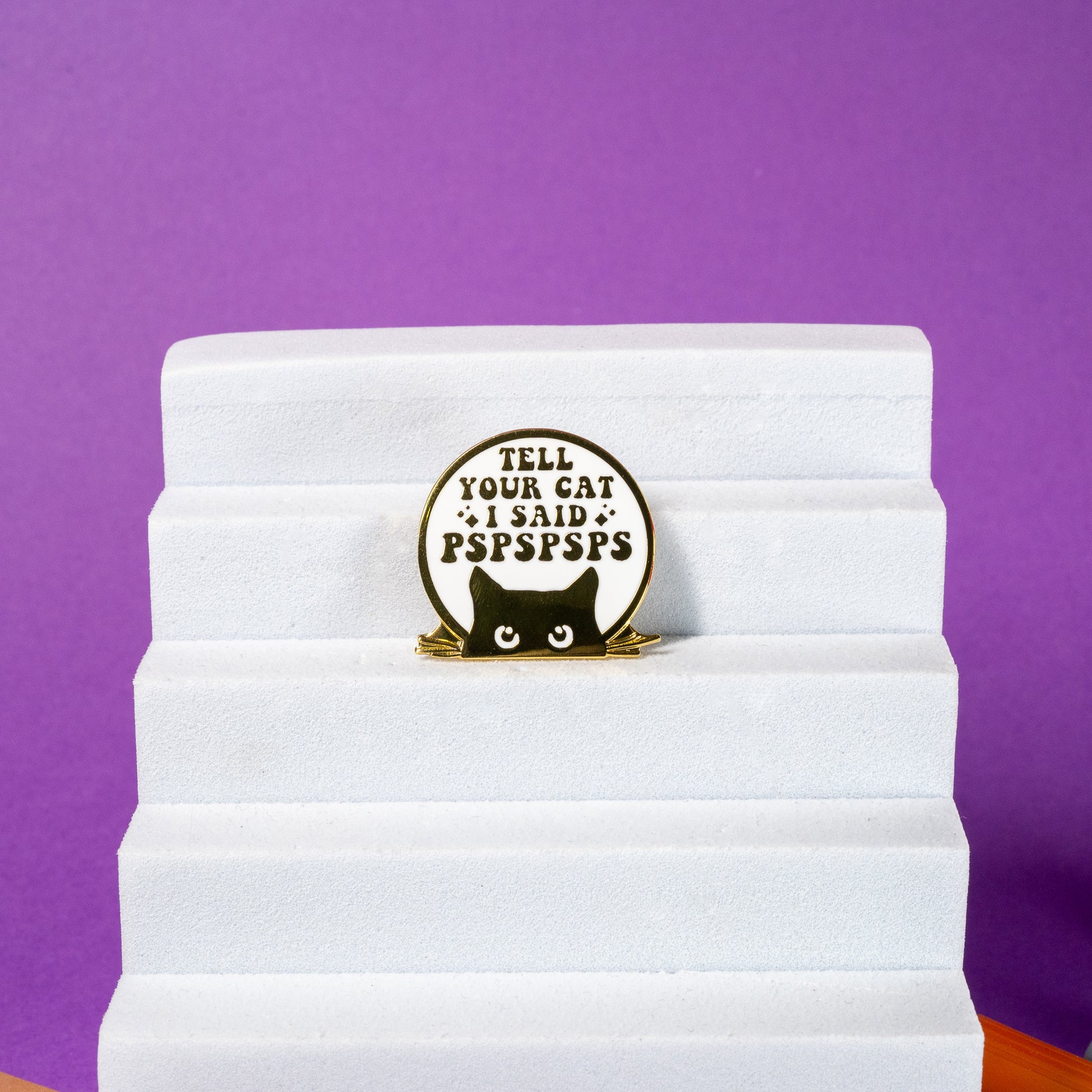 White and gold enamel pin featuring a cat face with the text Tell Your Cat I Said PSPSPSPS, perfect for cat lovers.