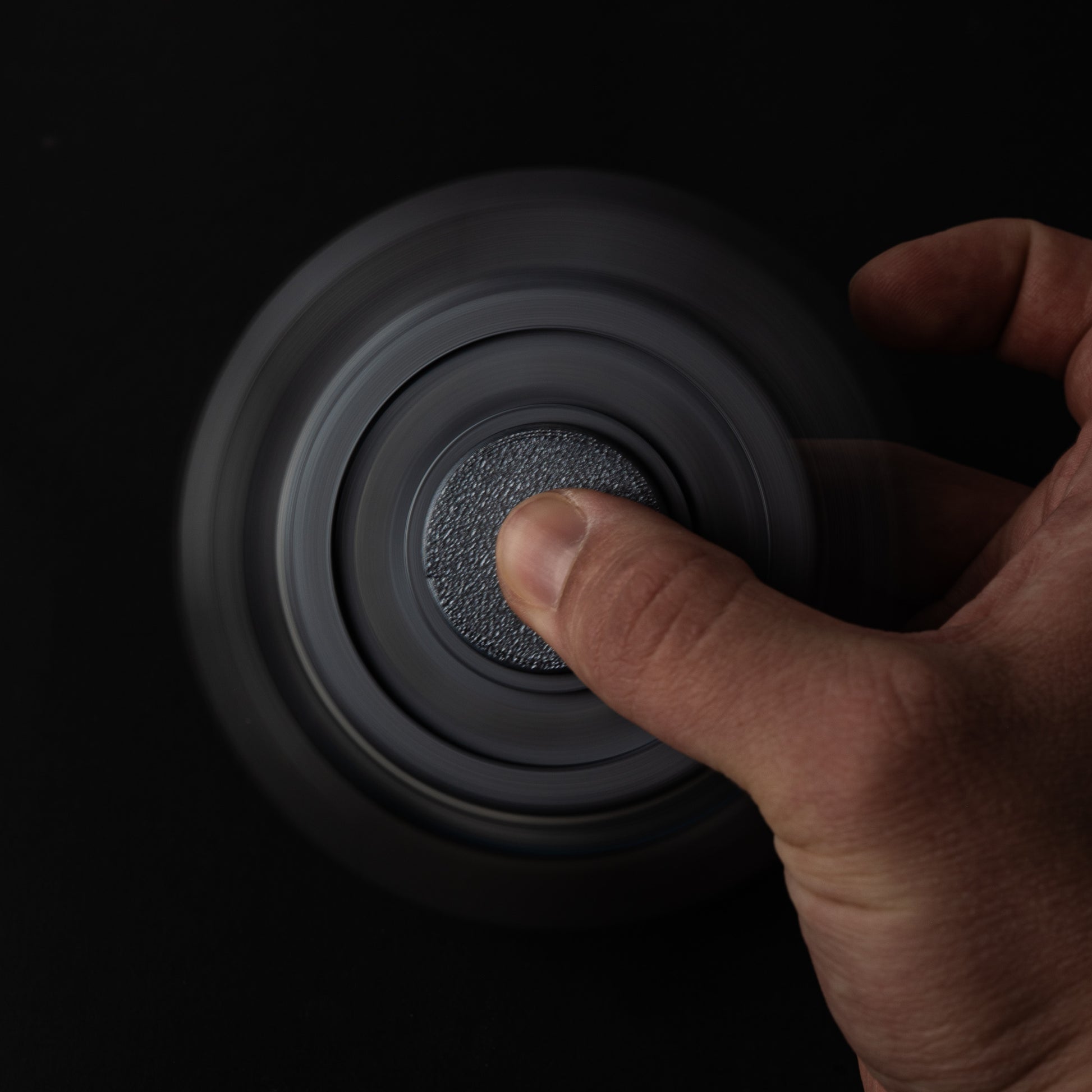 Gear fidget spinner in motion with smooth spin blur and tactile center grip under finger.
