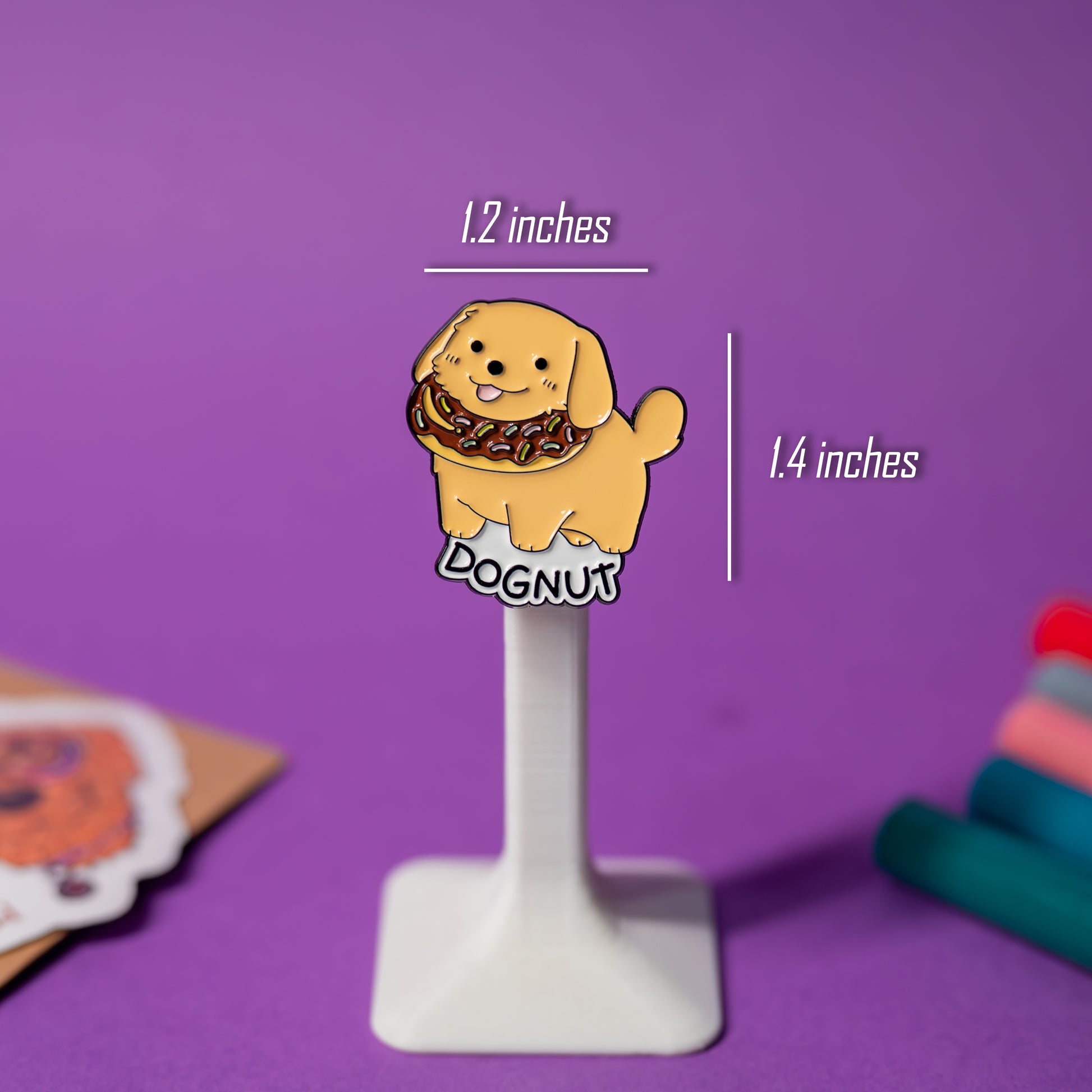 Close-up of DOGNUT enamel pin on clear plastic stand with size details visible.
