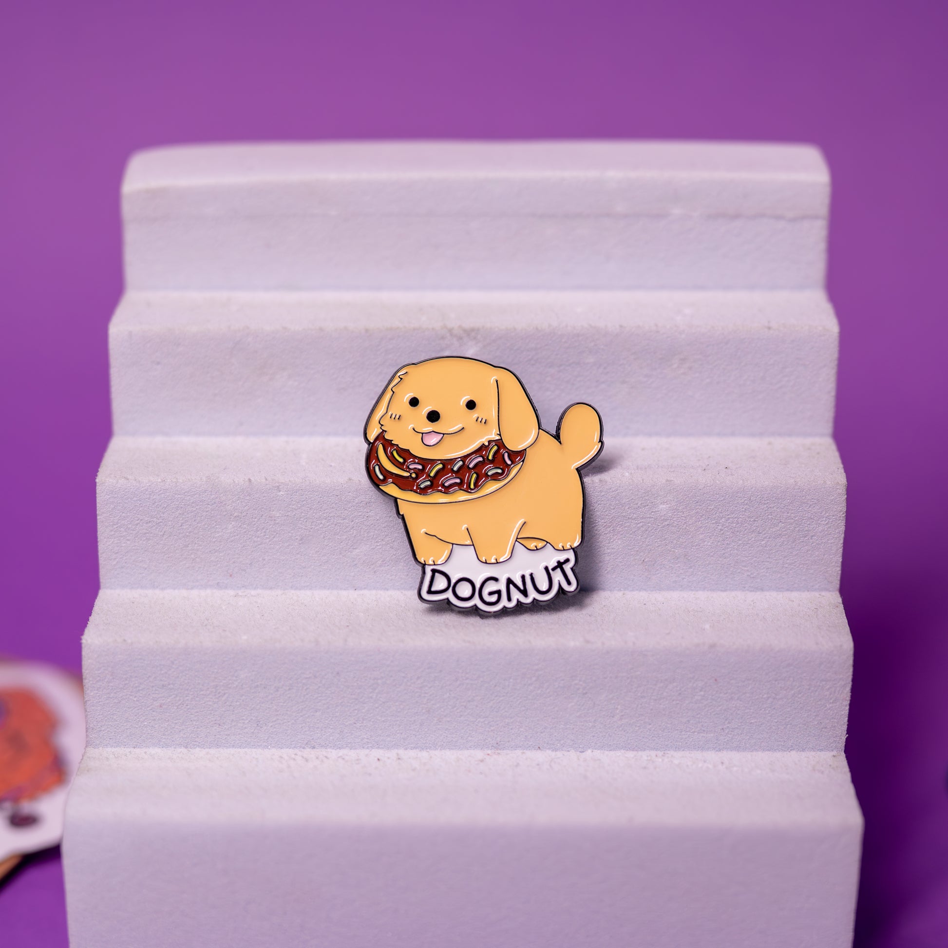 DOGNUT enamel pin displayed on foam stand, highlighting colors and playful dog-and-donut design.