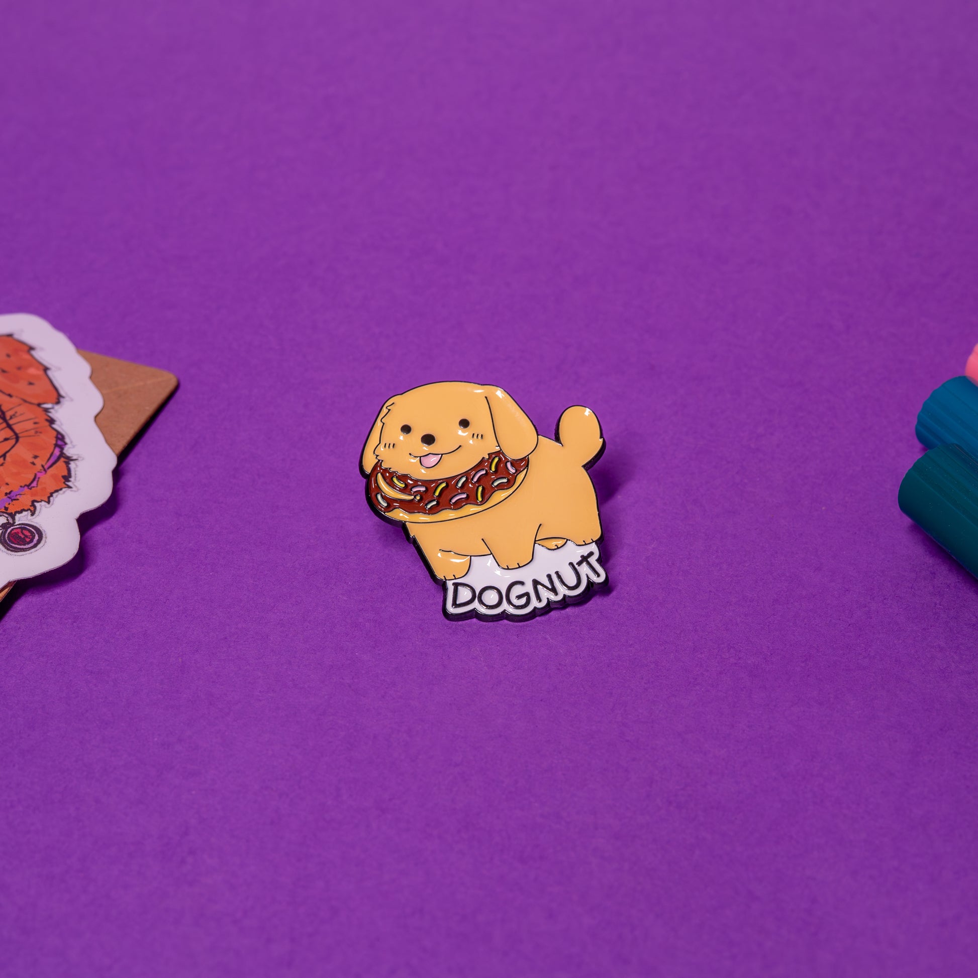 DOGNUT enamel pin featuring a cute dog with a donut collar, shown flat on table surface.