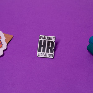 Walking HR Violation enamel pin shown flat on table, bold black and white work humor design.