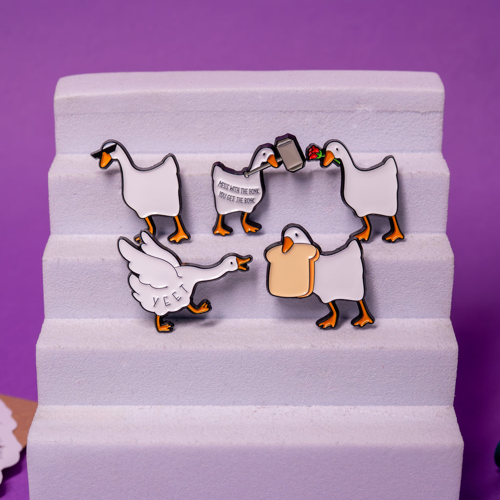 Set of 5 Untitled Goose enamel pins displayed on foam stand – Rose Goose, Bread Goose, Yeet Goose, Hammer Goose, Sunglasses Goose.