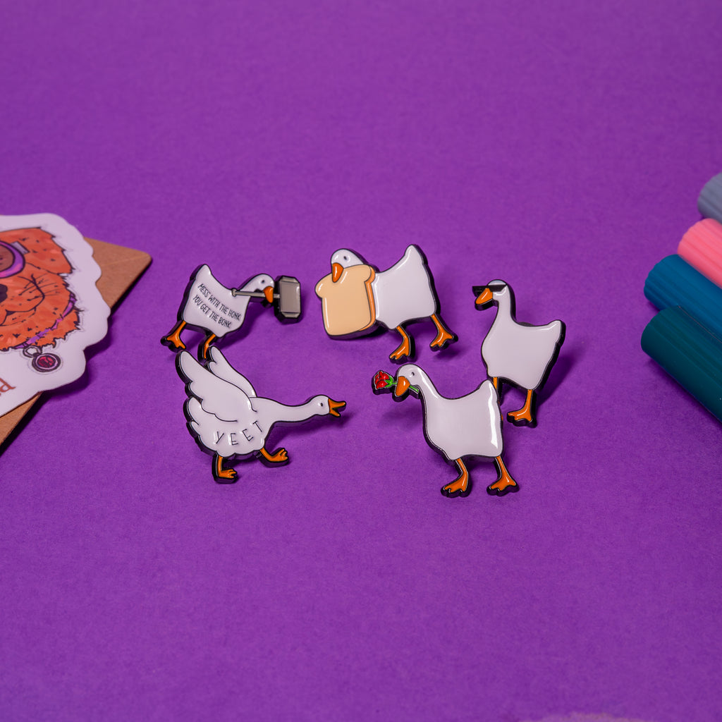 et of 5 Untitled Goose enamel pins laid flat on table – Rose Goose, Bread Goose, Yeet Goose, Hammer Goose, Sunglasses Goose.