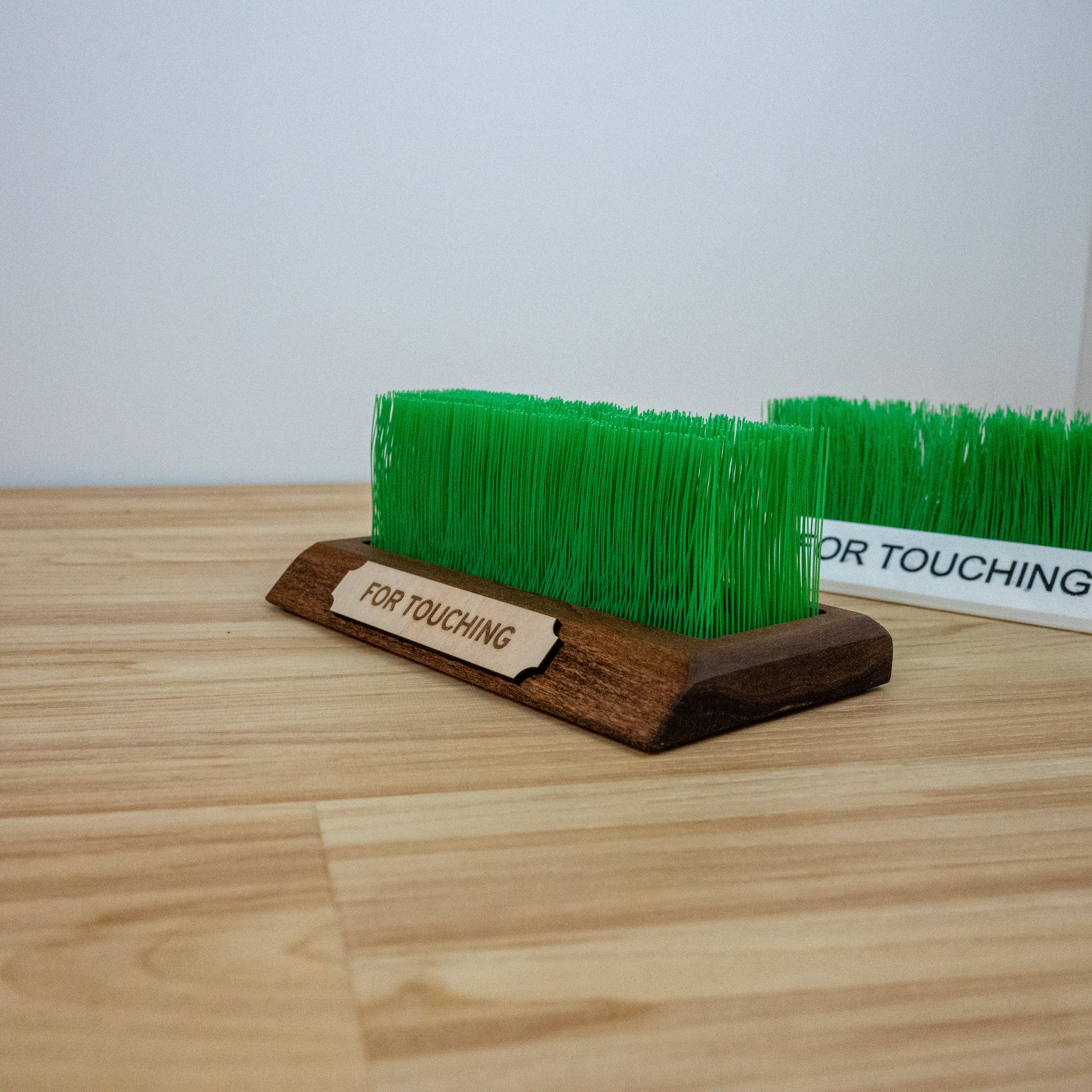 Side view of touch grass desk accessory showing “FOR TOUCHING” label on base