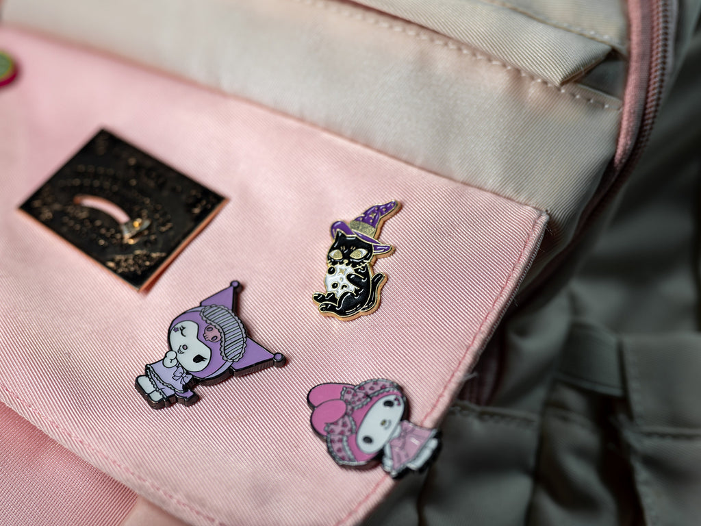 Magic Cat enamel pin featuring a black-and-gold cat in a witch hat holding a skull, styled on a backpack to showcase its versatility.