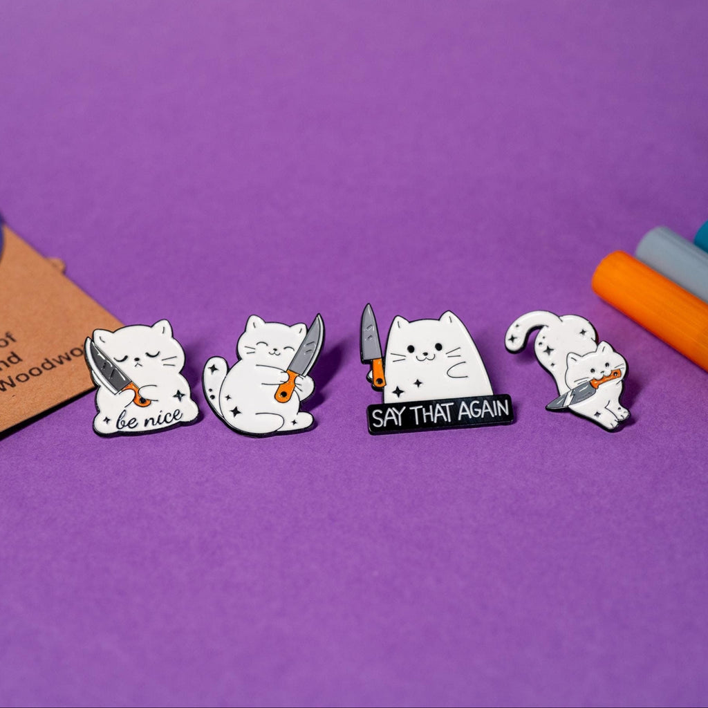Set of 4 white cat enamel pins featuring playful designs with cats and knives, including &#39;Say That Again,&#39; &#39;Be Nice,&#39; hugging knife, and jumping cat.
