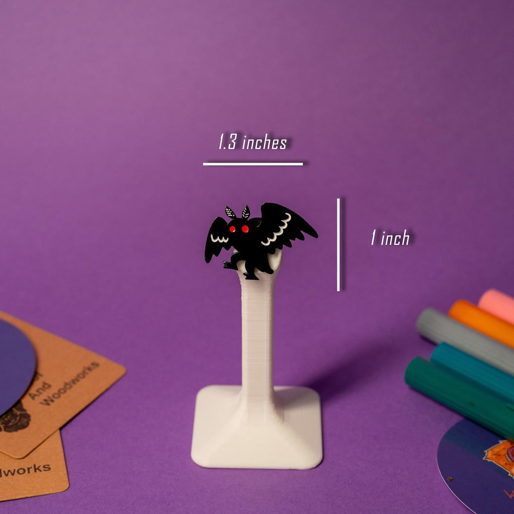 Mothman enamel pin displayed on a stand, highlighting the cryptid creature’s iconic silhouette.