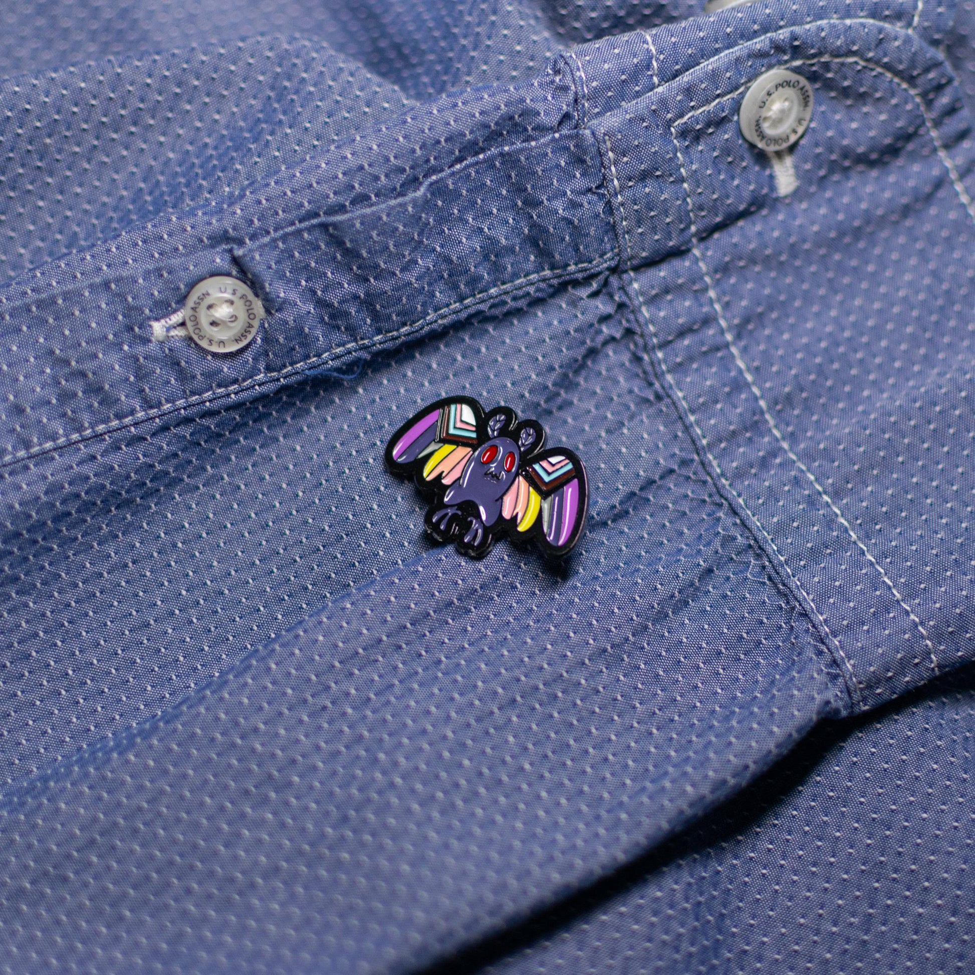 Mothman enamel pin with LGBTQ+ flag design displayed on a jacket, celebrating inclusivity and mystery.