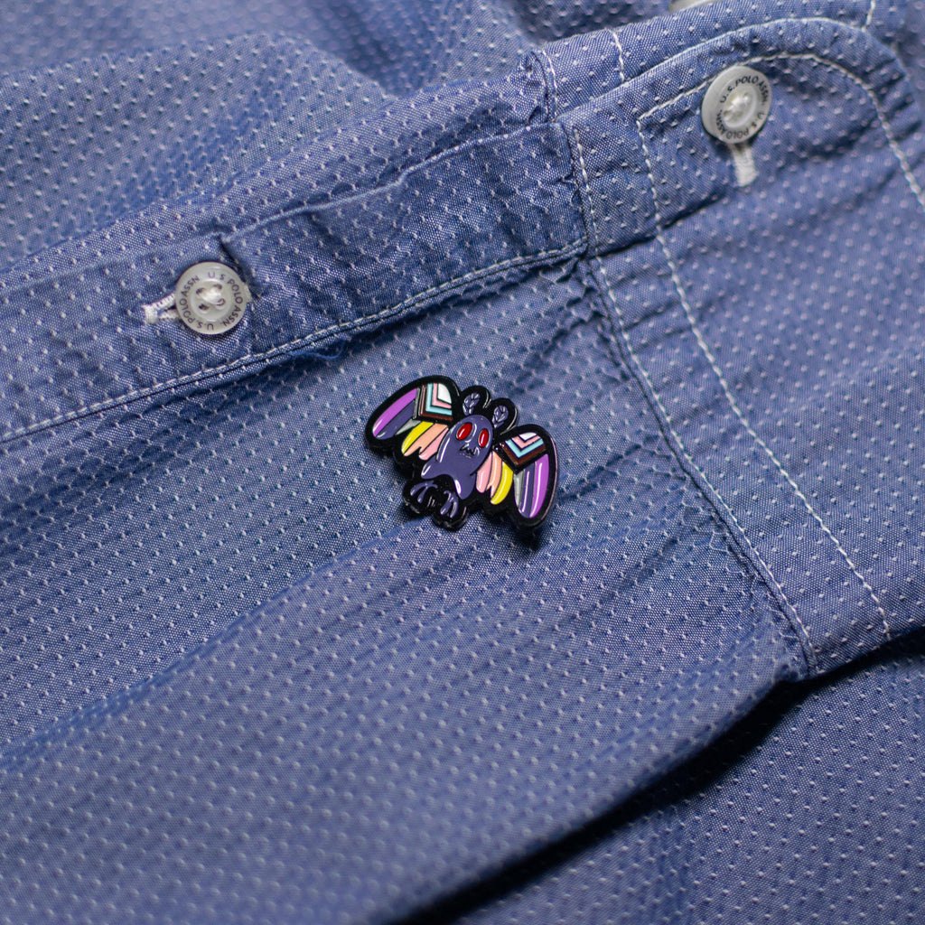Mothman enamel pin with LGBTQ+ flag design displayed on a jacket, celebrating inclusivity and mystery.