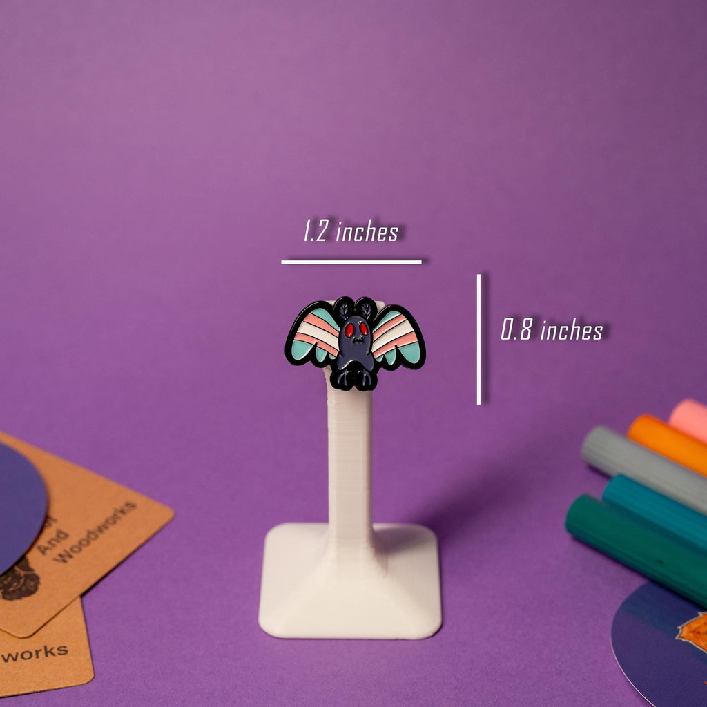 Close-up of Mothman enamel pin with Transgender pride flag design, showcasing bold colors and unique style.