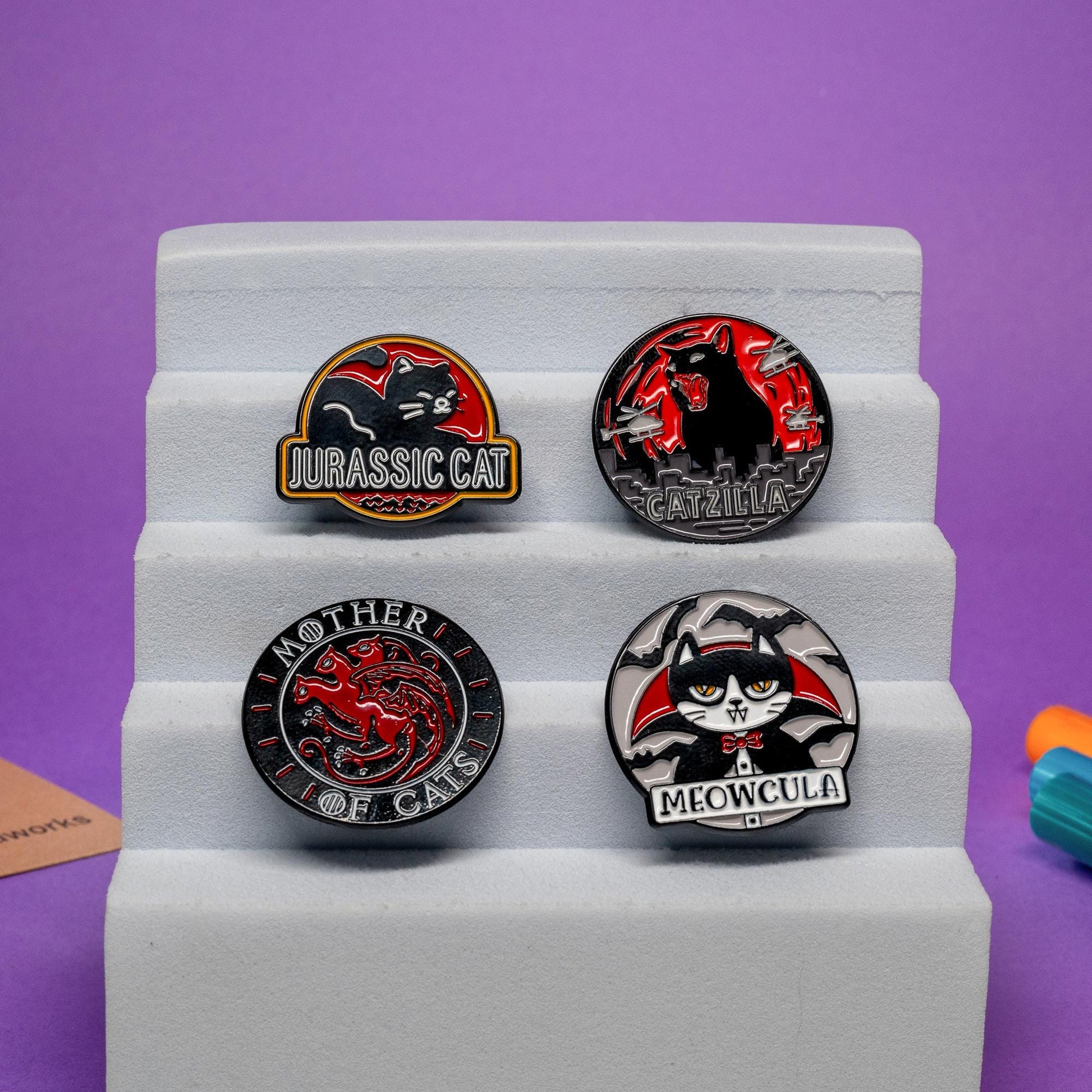 Set of 4 funny cat enamel pins featuring designs inspired by pop culture: Catzilla, Mother of Cats, Jurassic Cat, and Meowcula.