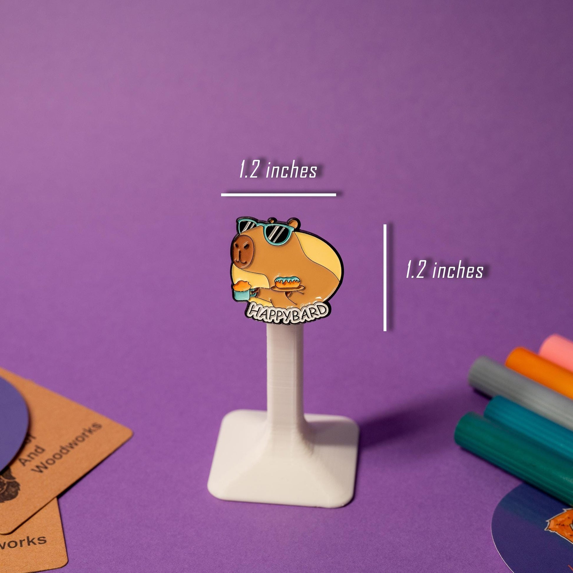 Enamel pin featuring a capybara with sunglasses holding coffee and a donut, with the text Happybard.