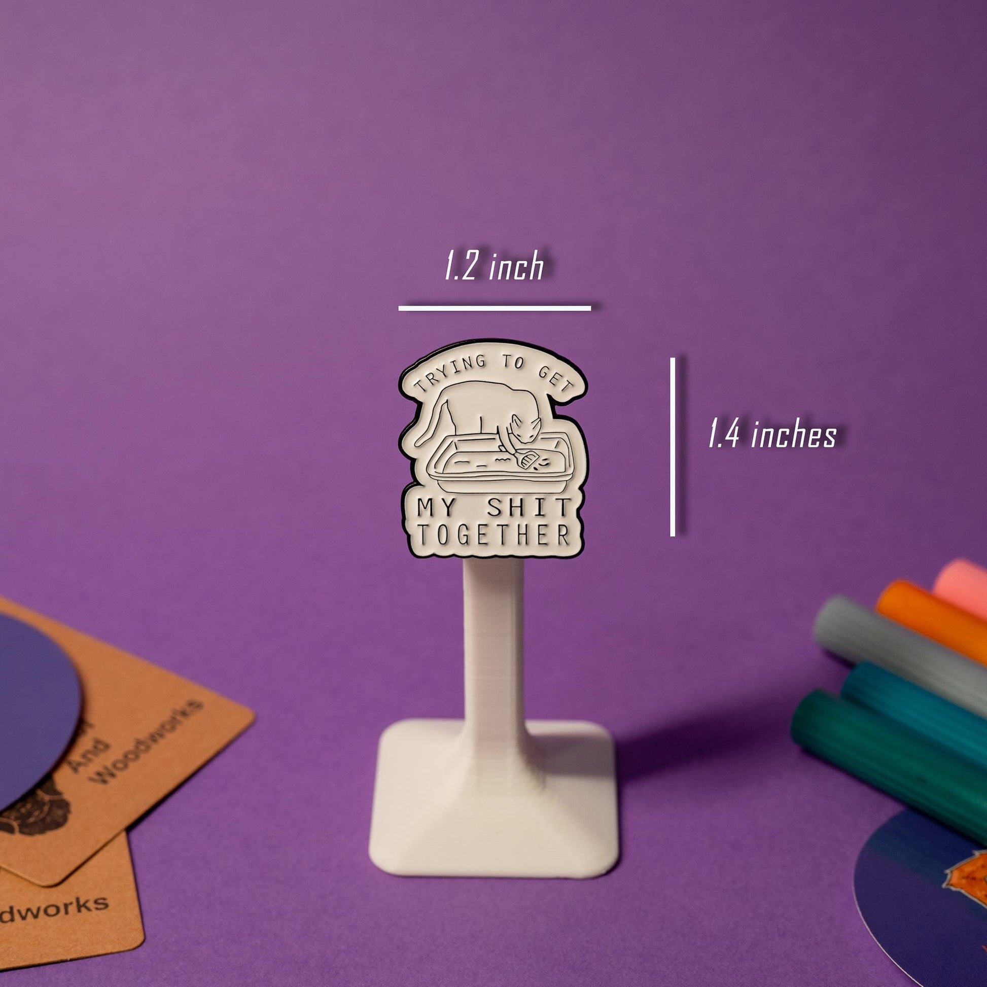 Close-up of enamel pin with a quirky cat scooping litter, showcasing the text Trying to get my sh*t together.