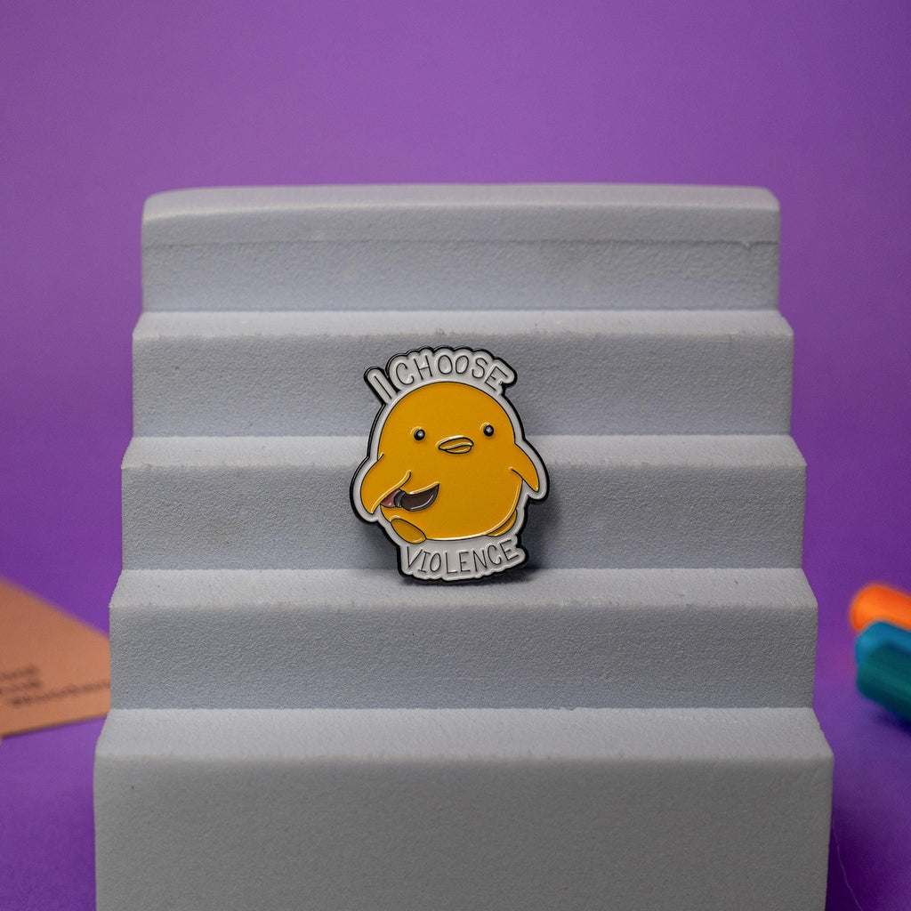 Close-up of a duck enamel pin with a knife and bold text I Choose Violence, great for quirky humor fans.