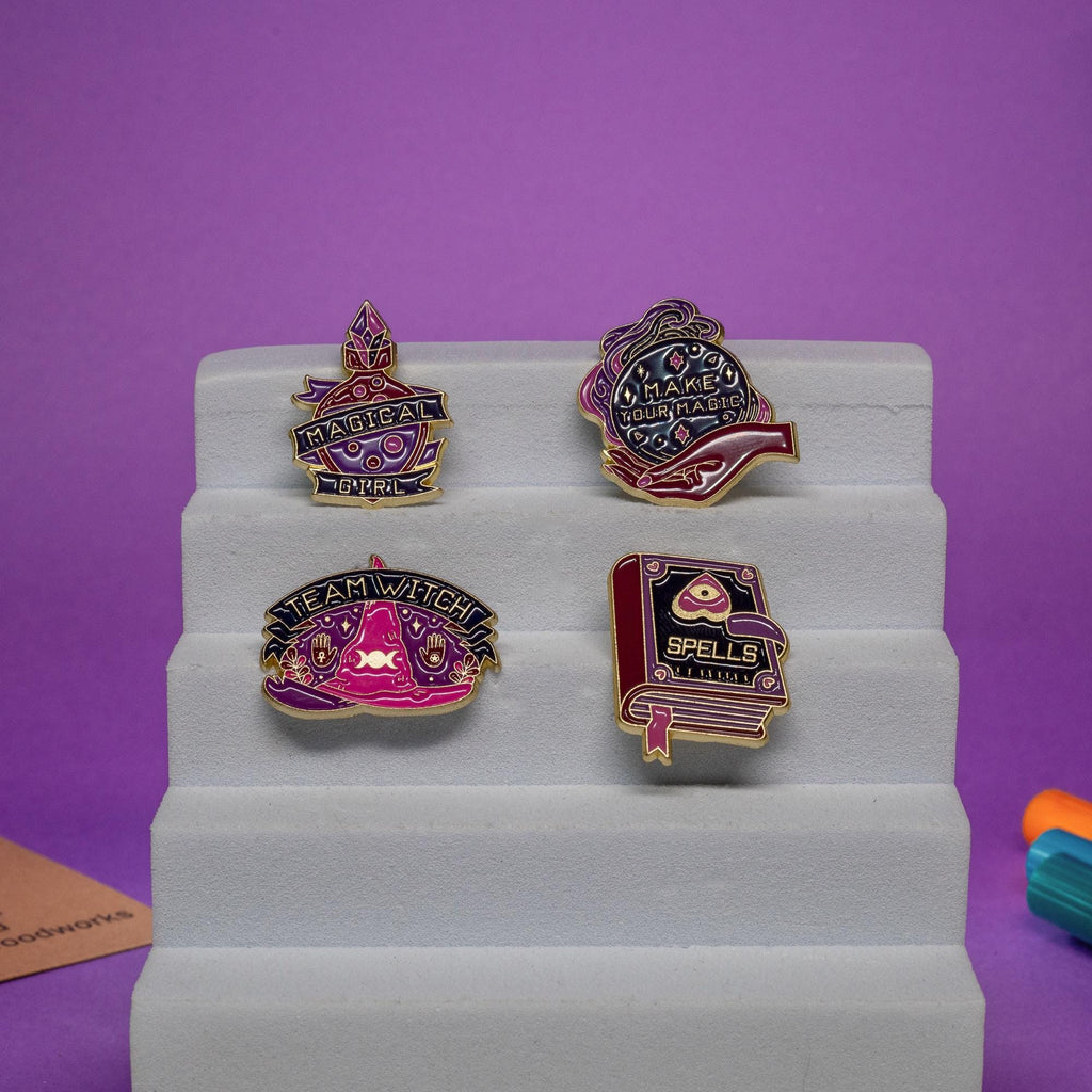 Group photo of 4 mystical enamel pins, including a witch hat, spell book, potion flask, and crystal ball hand.