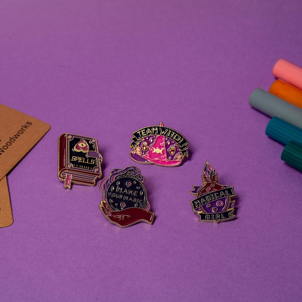 Set of 4 witchy enamel pins featuring Team Witch, Spells, Magic Girl, and Make Your Magic designs in a purple-pink aesthetic.