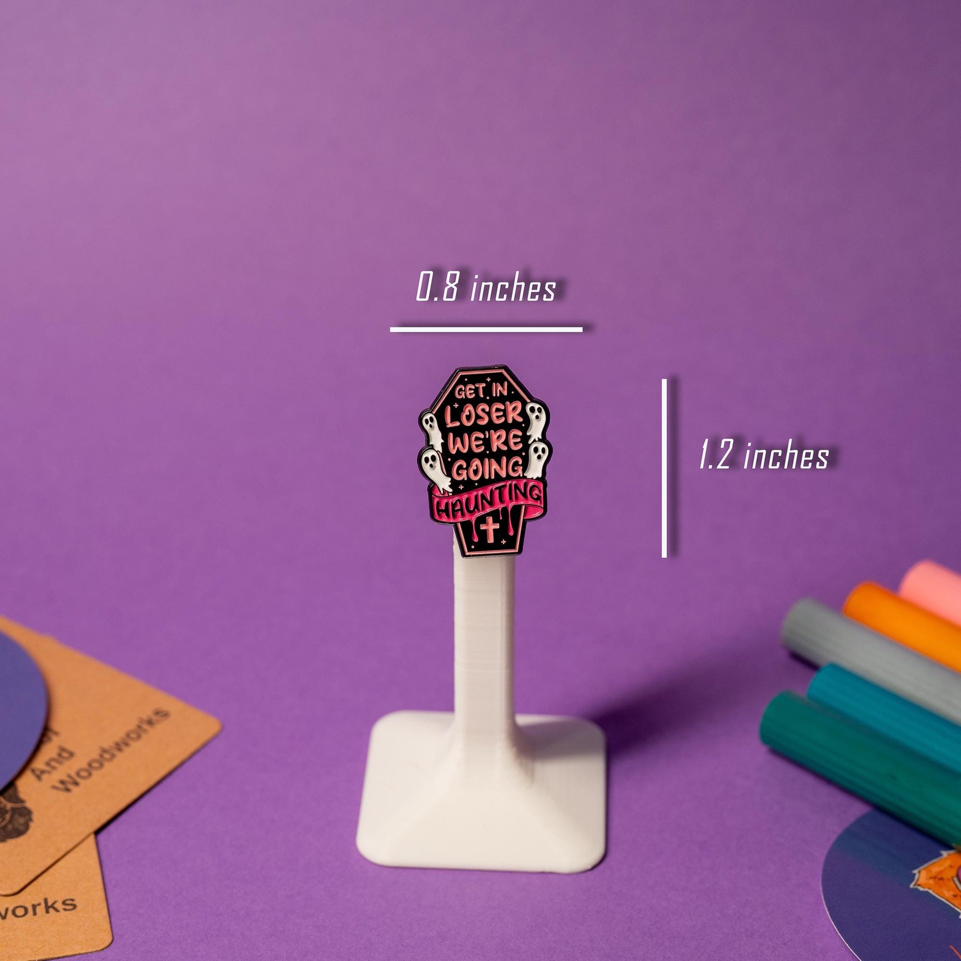 Coffin-shaped enamel pin featuring flying ghosts and the phrase Get In Loser, We’re Going Haunting.