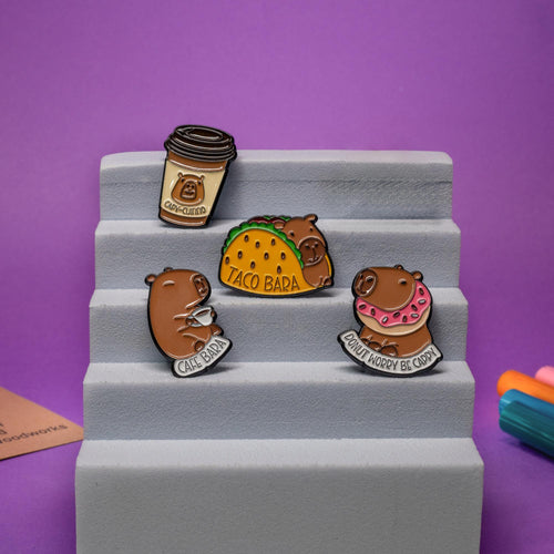 Capybara enamel pins displayed together, including Taco Bara and Donut Worry Be Cappy designs.