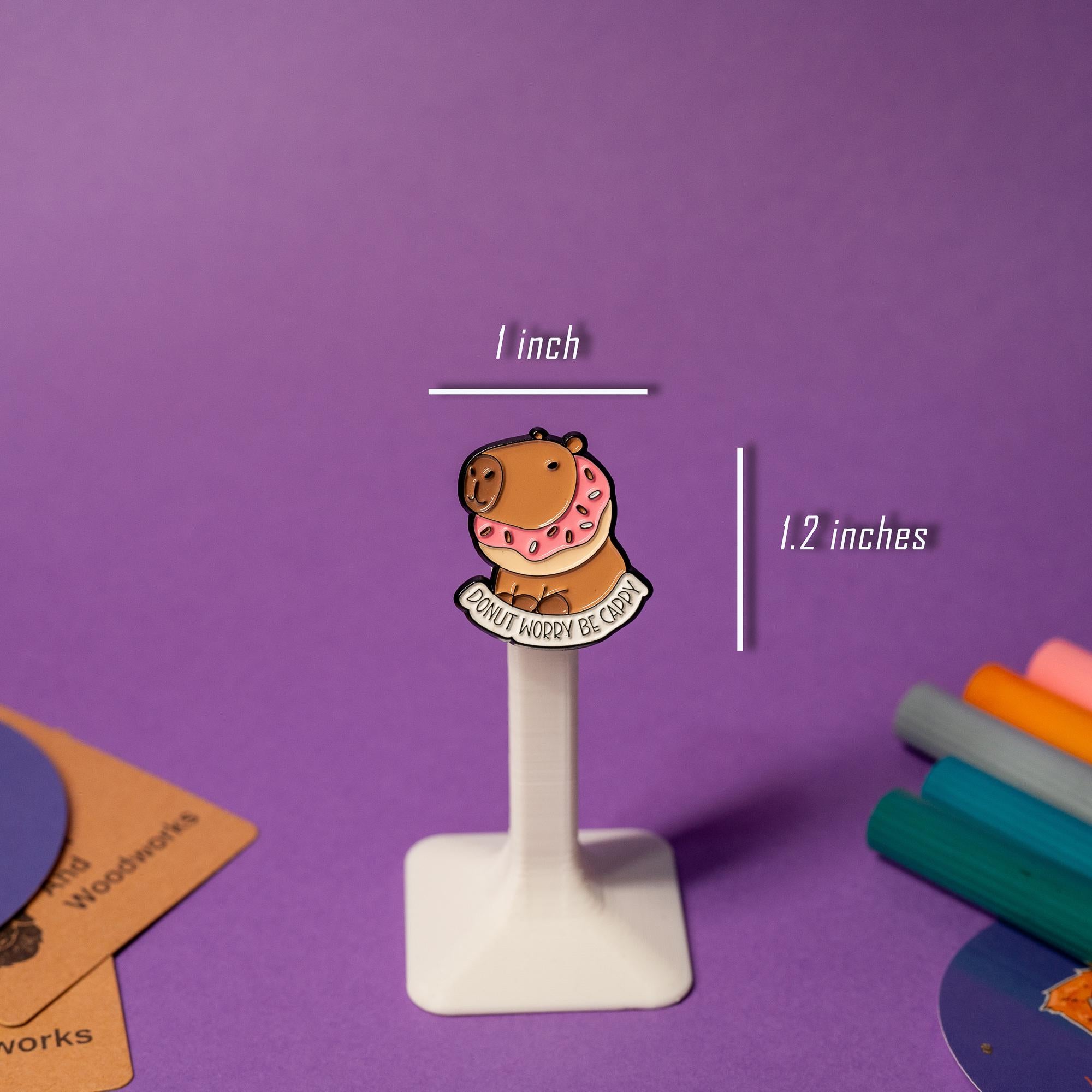 Close-up of the Donut Worry Be Cappy enamel pin, featuring a capybara holding a coffee cup.