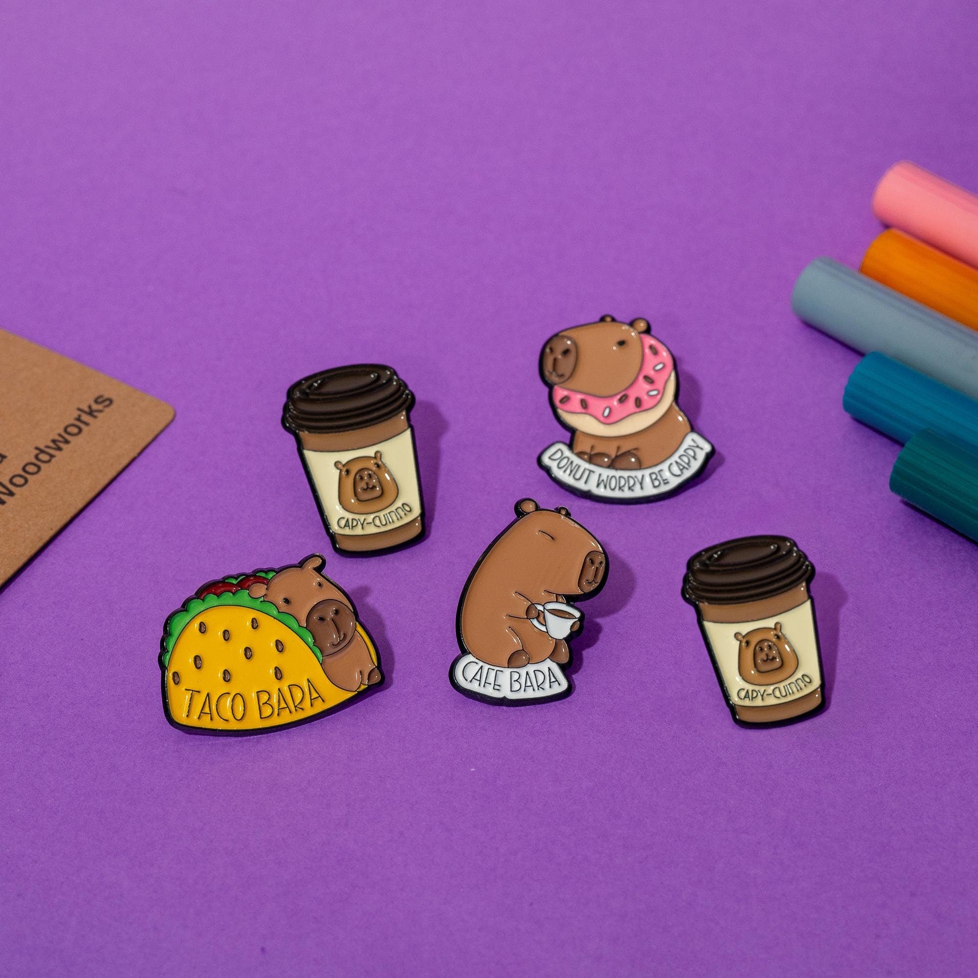 Set of 4 enamel pins featuring funny capybara designs, including Cafe Bara, Taco Bara, Donut Worry, and Capy-Cuino.