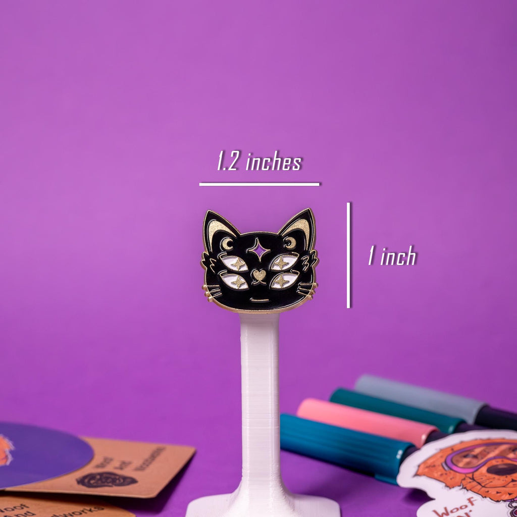 Close-up of a four-eyed black-and-gold cat face enamel pin with moon symbols, showcasing its mystic and elegant design.