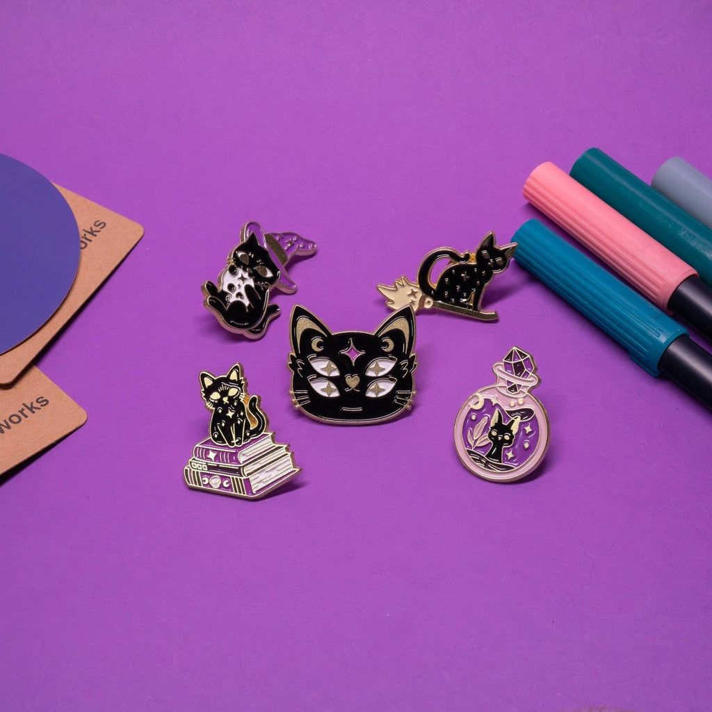 Full set of five Magic Cat enamel pins displayed together, featuring black-and-gold cats with purple accents in various witchy designs.