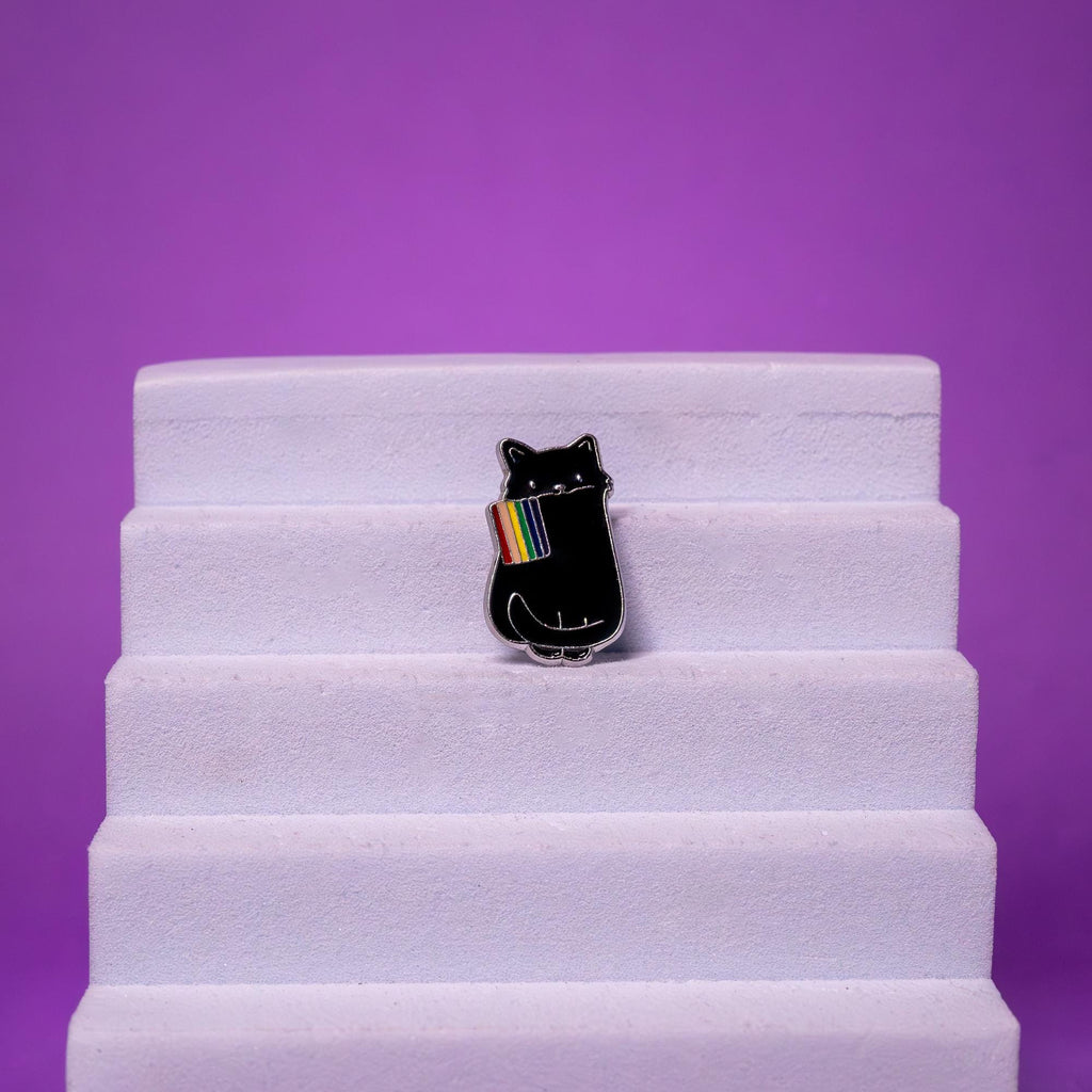 LGBTQ Pride enamel pin featuring a black cat with a rainbow flag, displayed on a foam stand to emphasize its craftsmanship and presentation.
