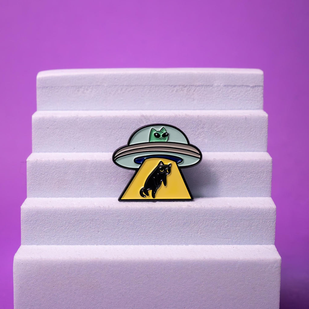 Alien cat enamel pin displayed on a foam stand, highlighting its vibrant green, black, and yellow colors and unique sci-fi design.