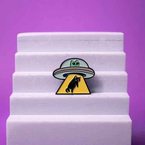 Alien cat enamel pin displayed on a foam stand, highlighting its vibrant green, black, and yellow colors and unique sci-fi design.