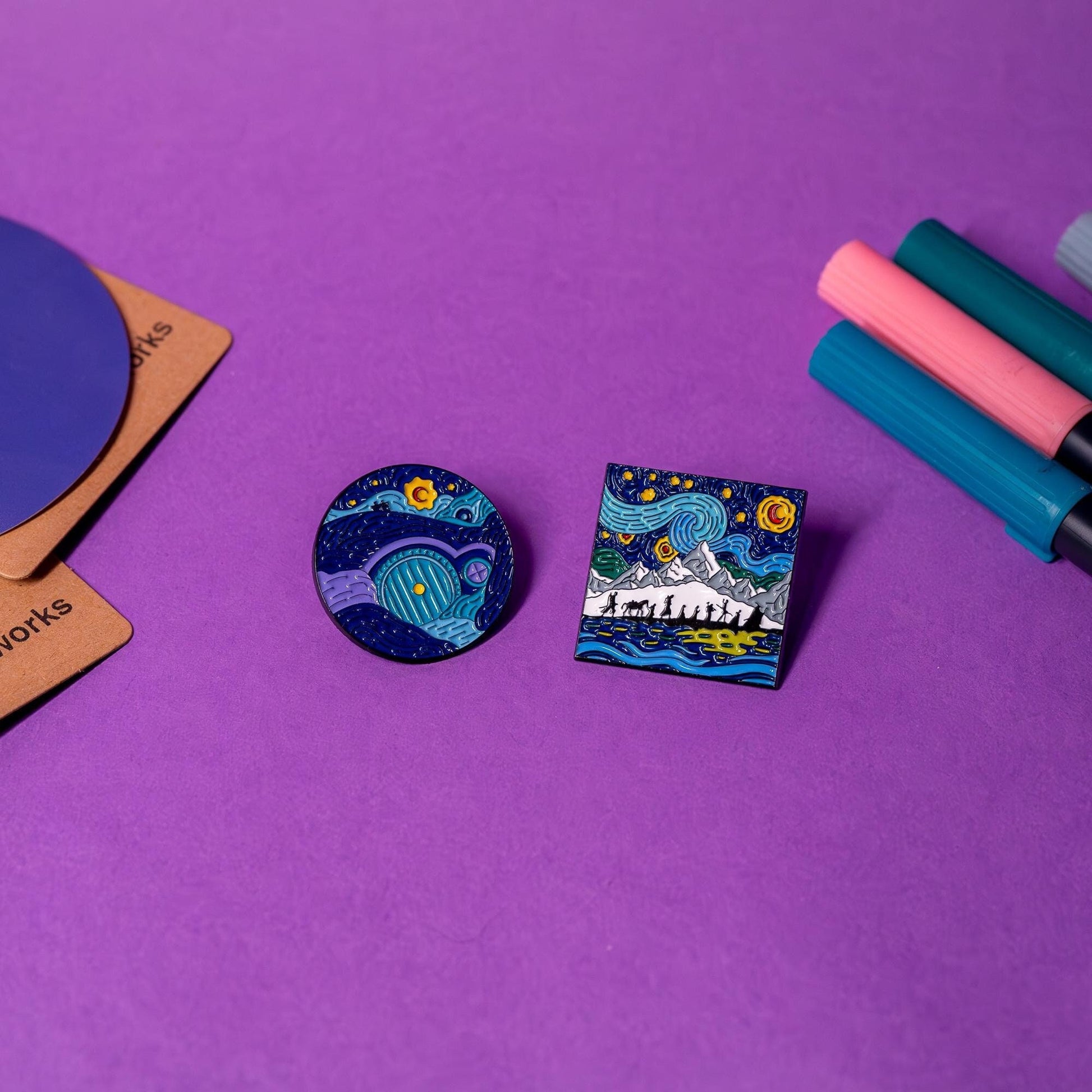 Lord of the Rings enamel pins displayed on a flat surface, featuring the Fellowship under Starry Skies and the Hobbit’s door in Van Gogh-inspired designs.