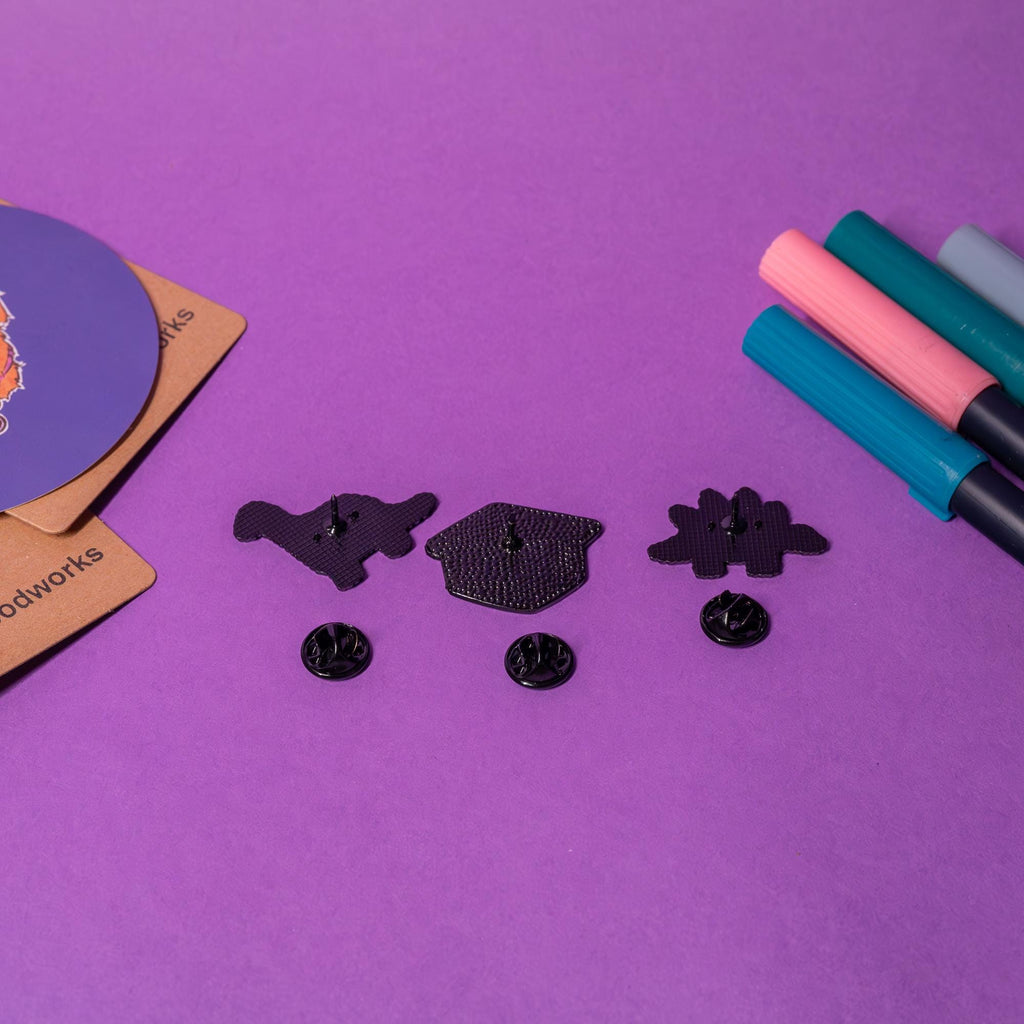 Back view of the Dino Nugget enamel pin set, showing smooth metal finishes and secure butterfly clasps for all three pins.