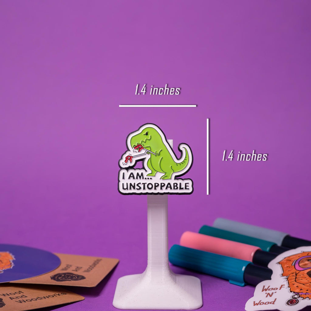 Close-up of the Unstoppable T-Rex enamel pin, showcasing the playful dinosaur design with extended arms and bold text.
