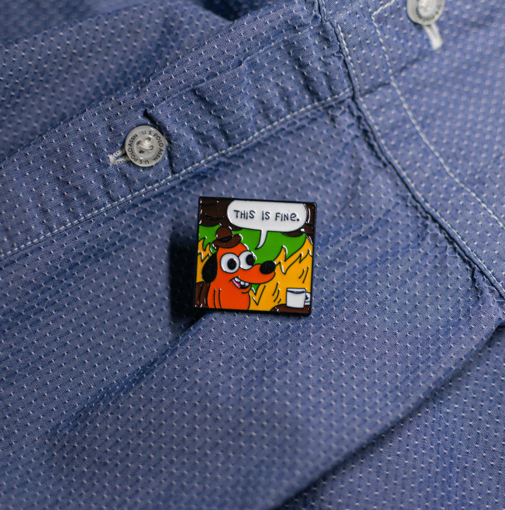 Funny enamel pin of the This Is Fine meme, displayed on a jacket, ideal for quirky and relatable accessories.