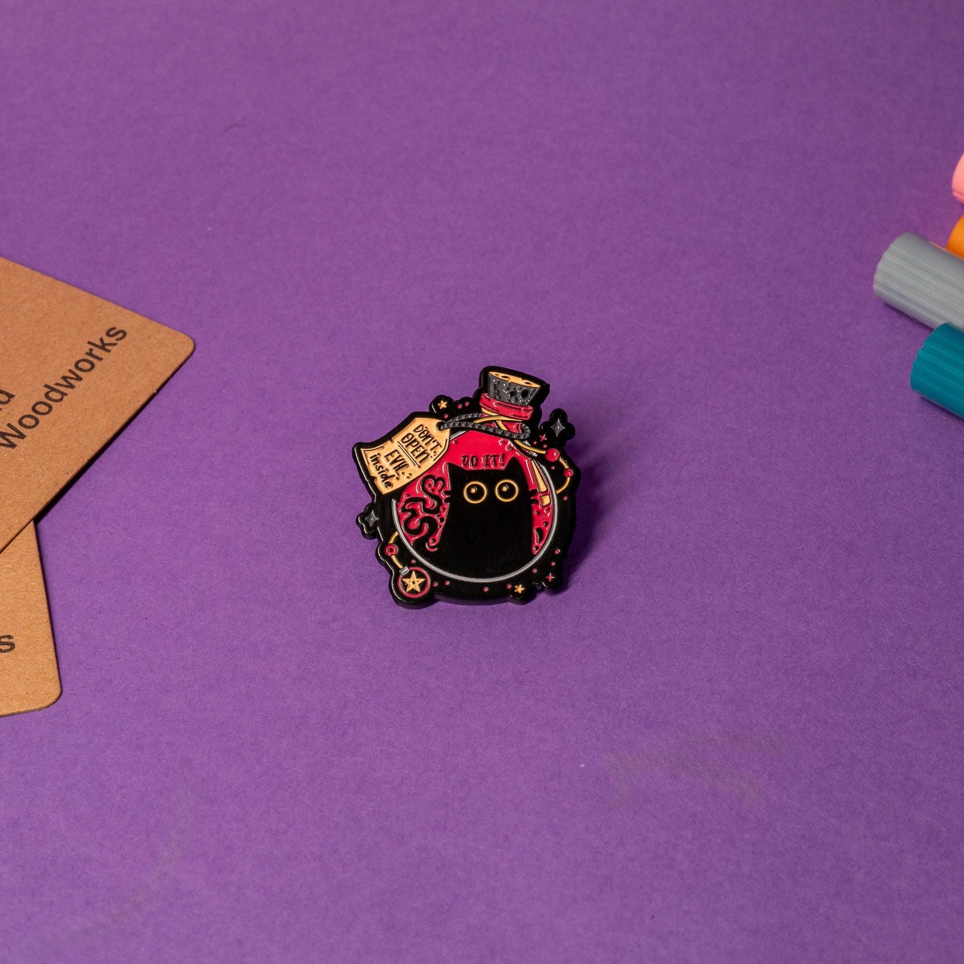 Close-up of enamel pin showcasing a black cat inside a magical flask with Do It and Don’t Open – Evil Inside warnings.