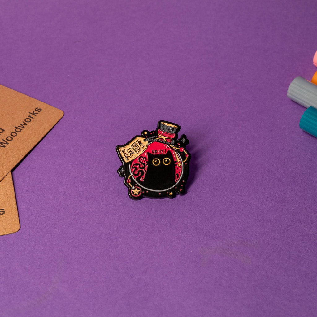 Close-up of enamel pin showcasing a black cat inside a magical flask with Do It and Don’t Open – Evil Inside warnings.