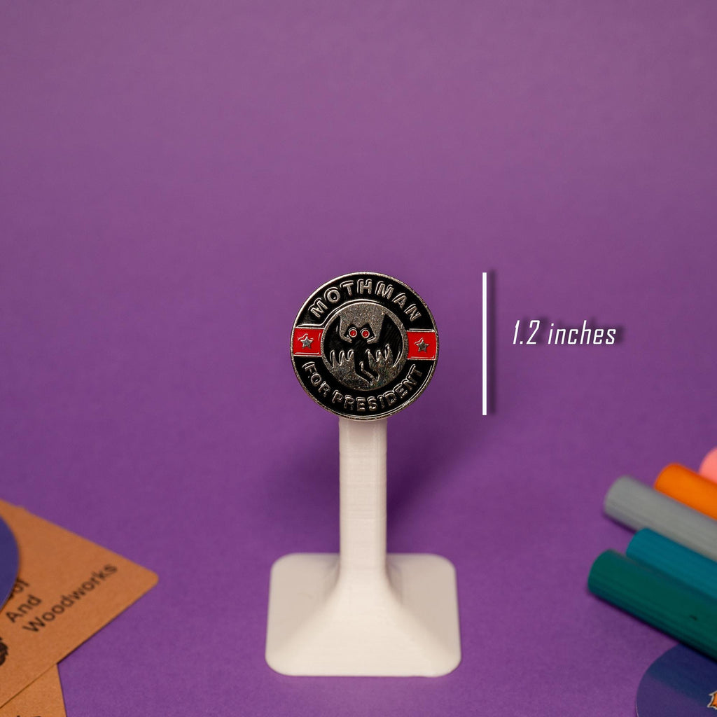 Mothman enamel pin displayed on a stand, showcasing the text Mothman For President in bold letters.
