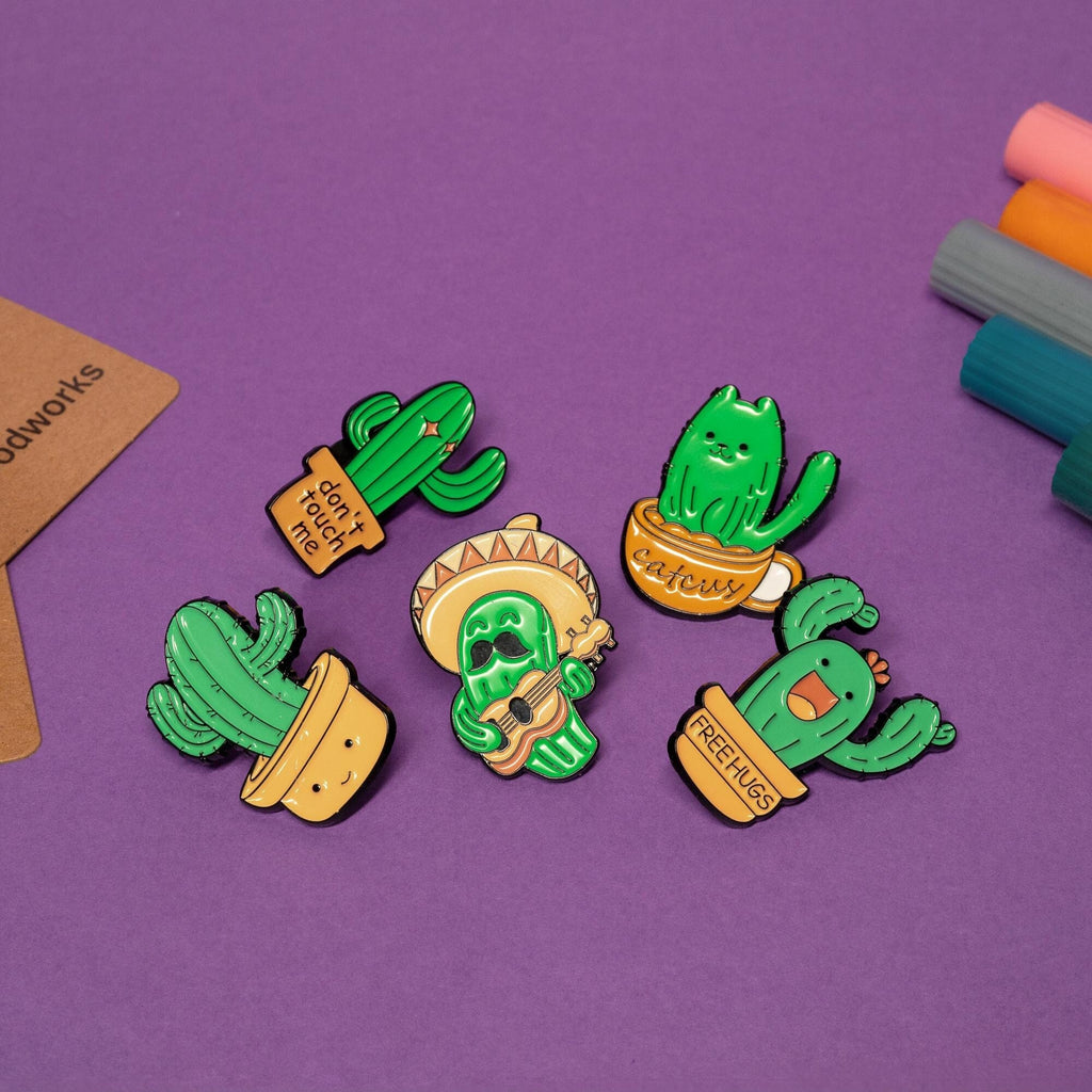 Set of 5 funny cactus enamel pins featuring unique designs: Free Hugs, Don’t Touch Me, Catcus, sombrero cactus, and smiling potted cactus.