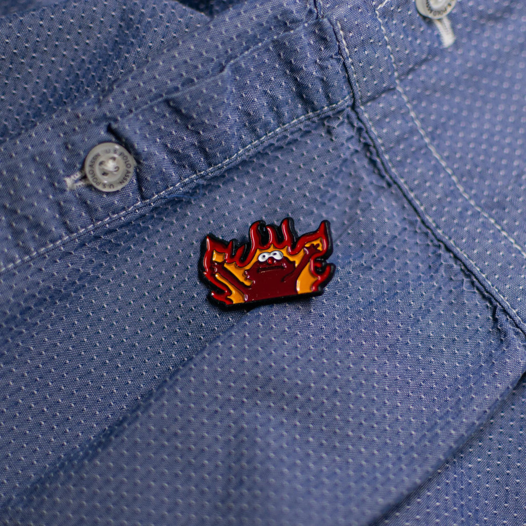 Close-up of the Hellmo enamel pin featuring the iconic fire puppet meme, showcasing bright red and orange flames with bold detailing.