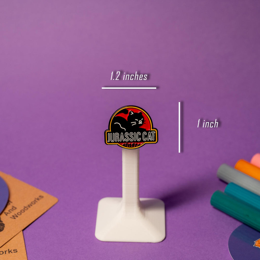 Parody enamel pin of the Jurassic Park logo with a black cat silhouette and the text Jurassic Cat.