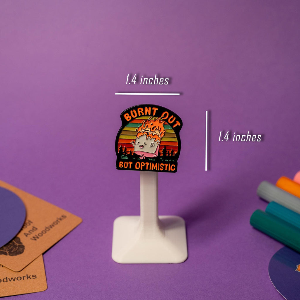 Enamel pin featuring a marshmallow running on fire with the humorous text Burnt Out but Optimistic.
