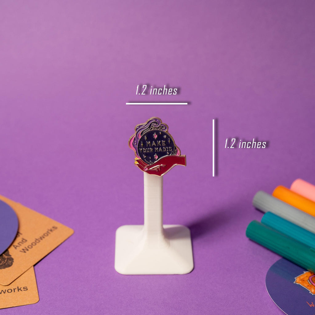 Purple-pink enamel pin featuring a hand holding a crystal ball with the phrase Make Your Magic.