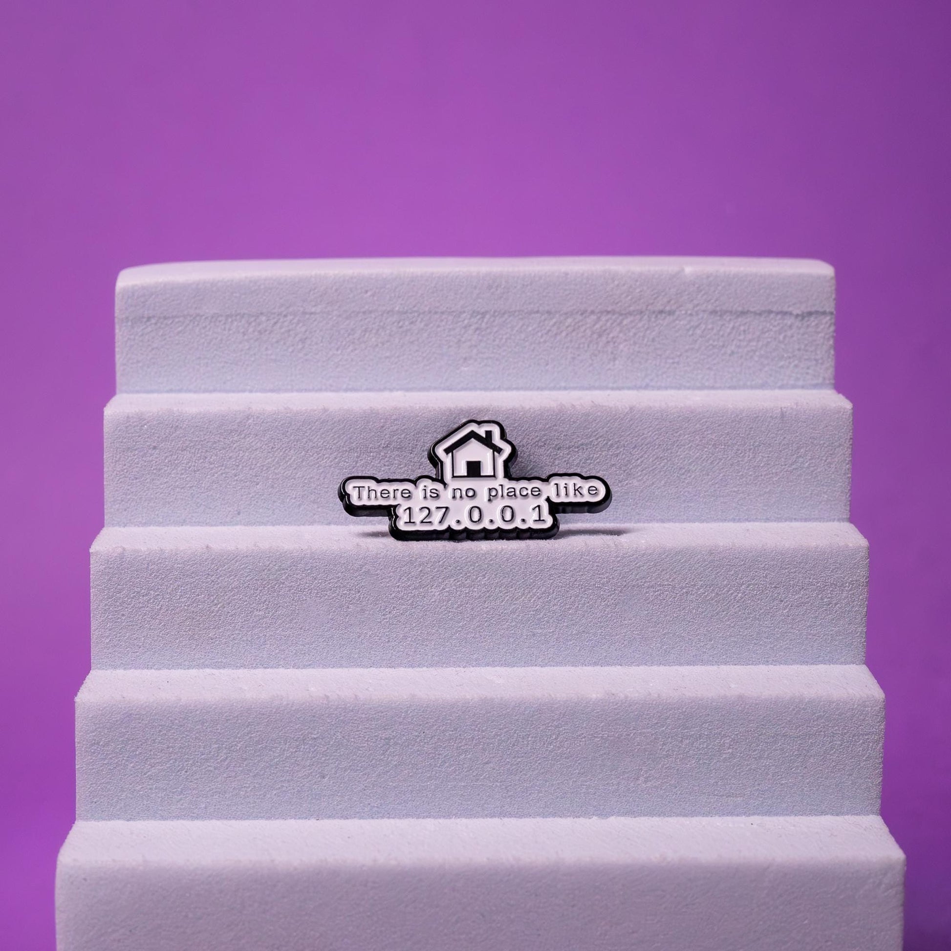 Enamel pin with the phrase There is no place like 127.0.0.1, displayed on a foam stand to emphasize its quality craftsmanship and geeky design.