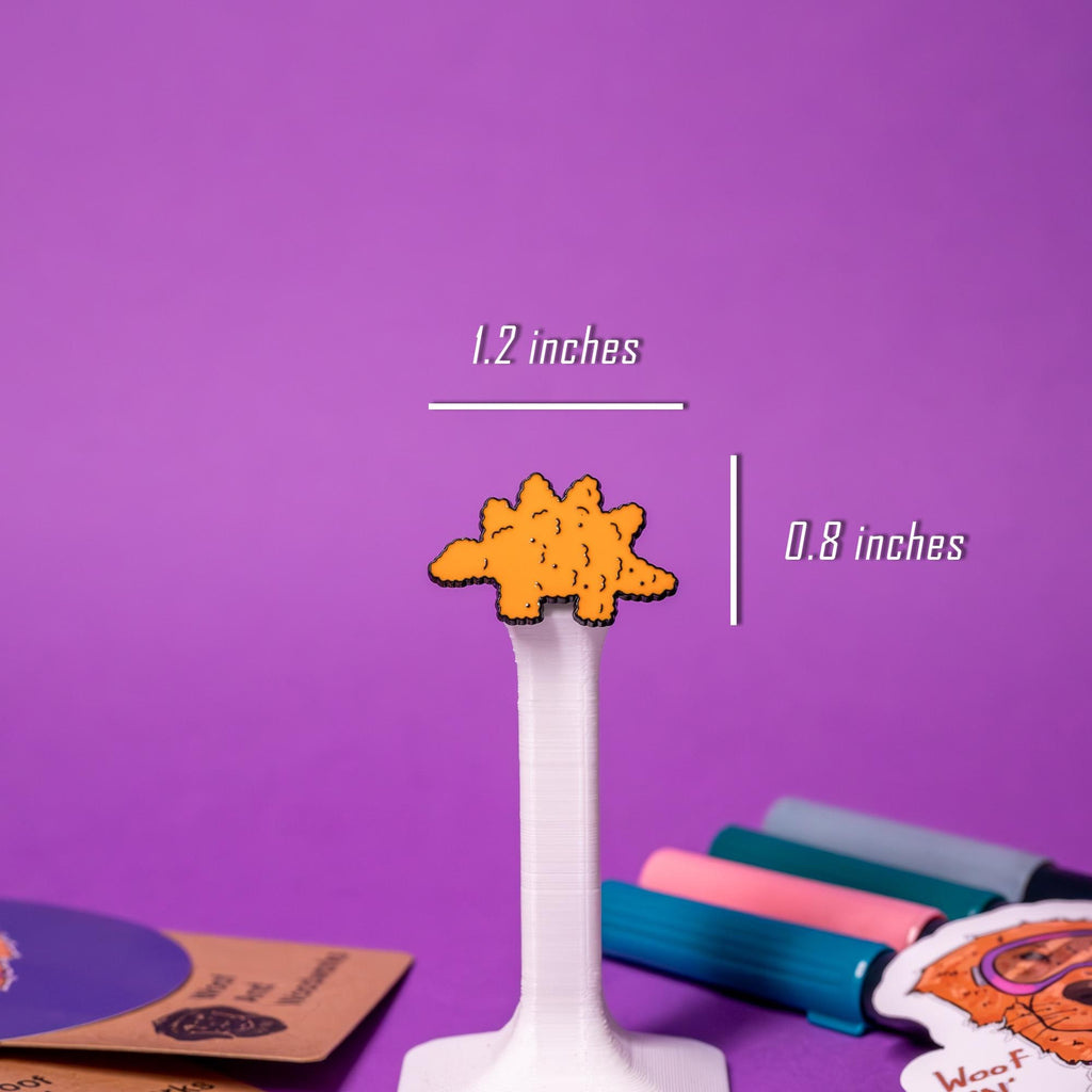 Close-up of the stegosaurus dino nugget enamel pin, highlighting its playful design and crispy nugget texture.