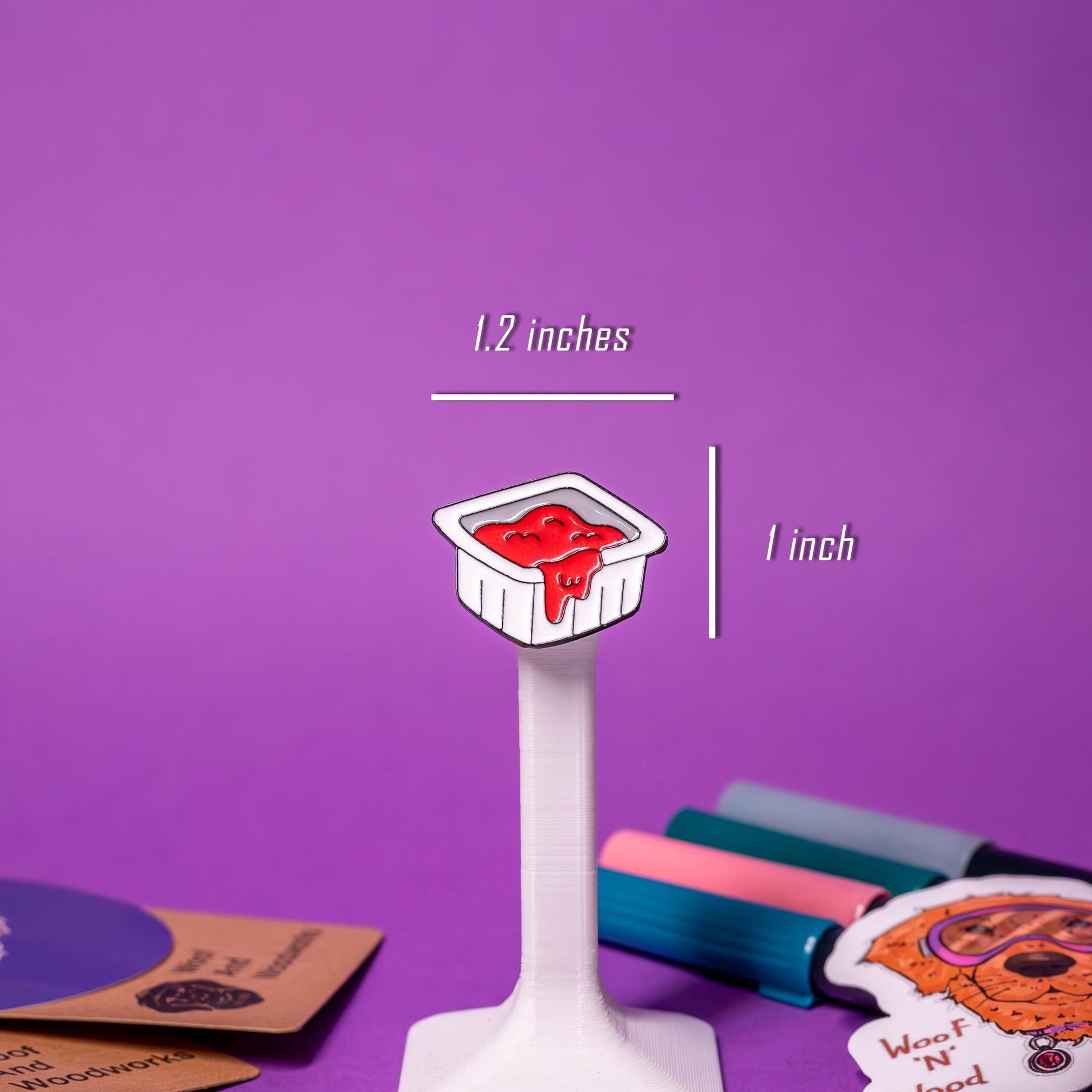 Close-up of the fast-food-style ketchup packet enamel pin, featuring a bright red design and peel-back detail.