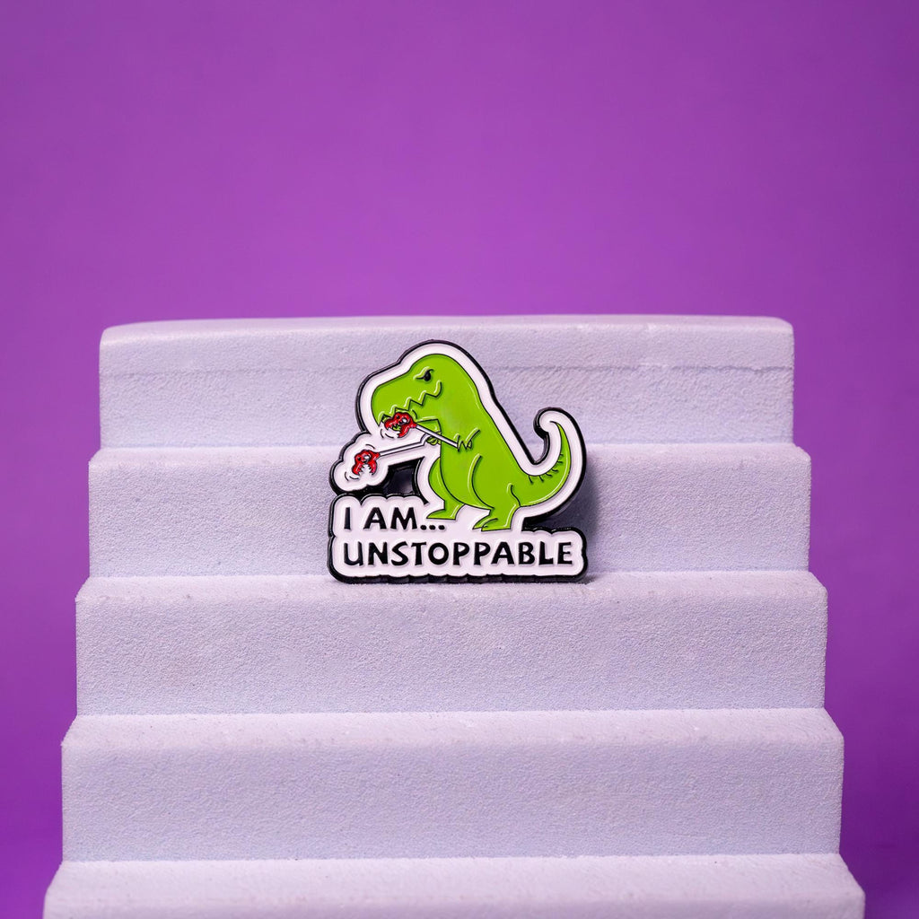 Unstoppable T-Rex enamel pin displayed on a foam stand, emphasizing its vibrant colors and humorous details.