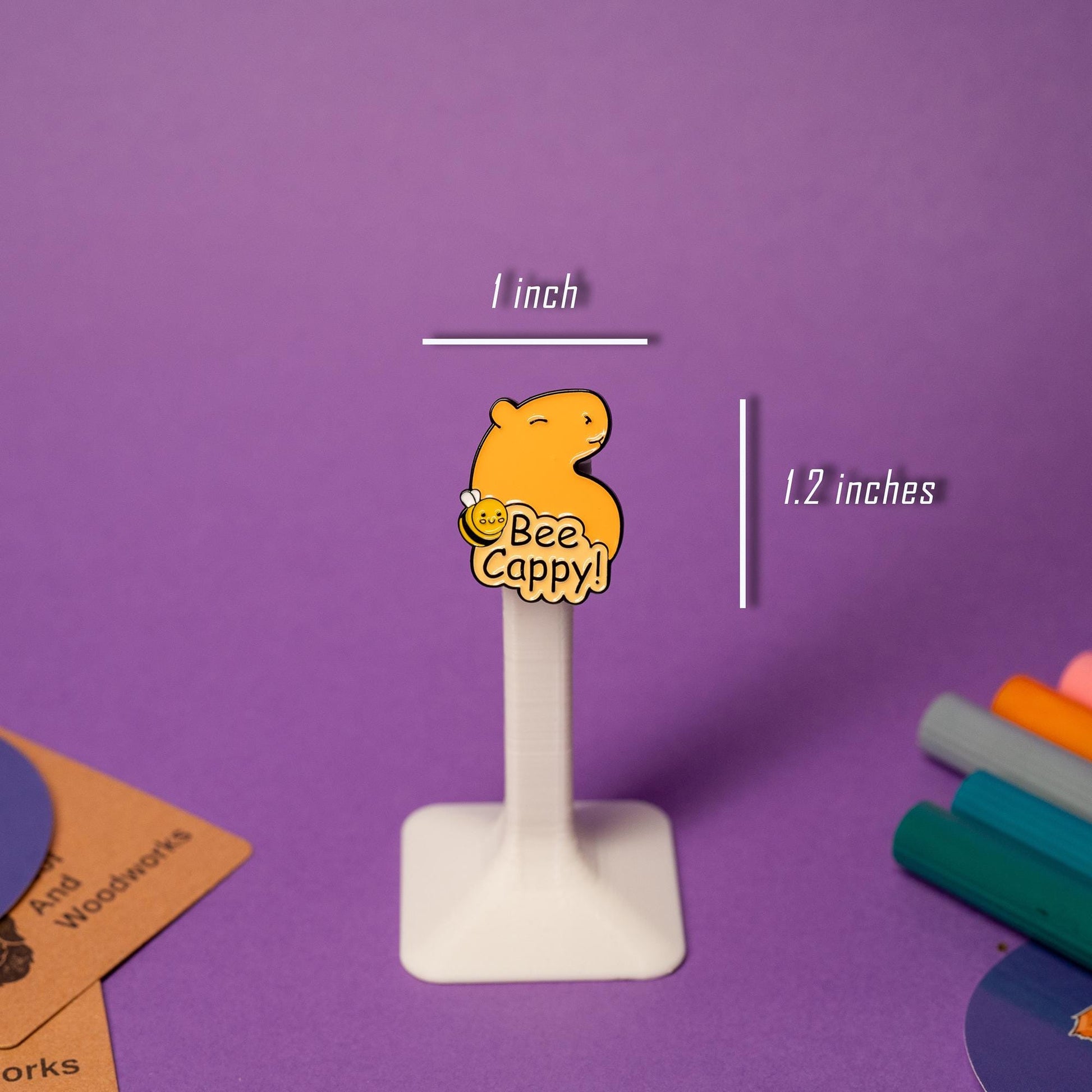Close-up of the Bee Cappy! enamel pin, featuring a cheerful capybara with a bee-themed design and bright yellow accents.